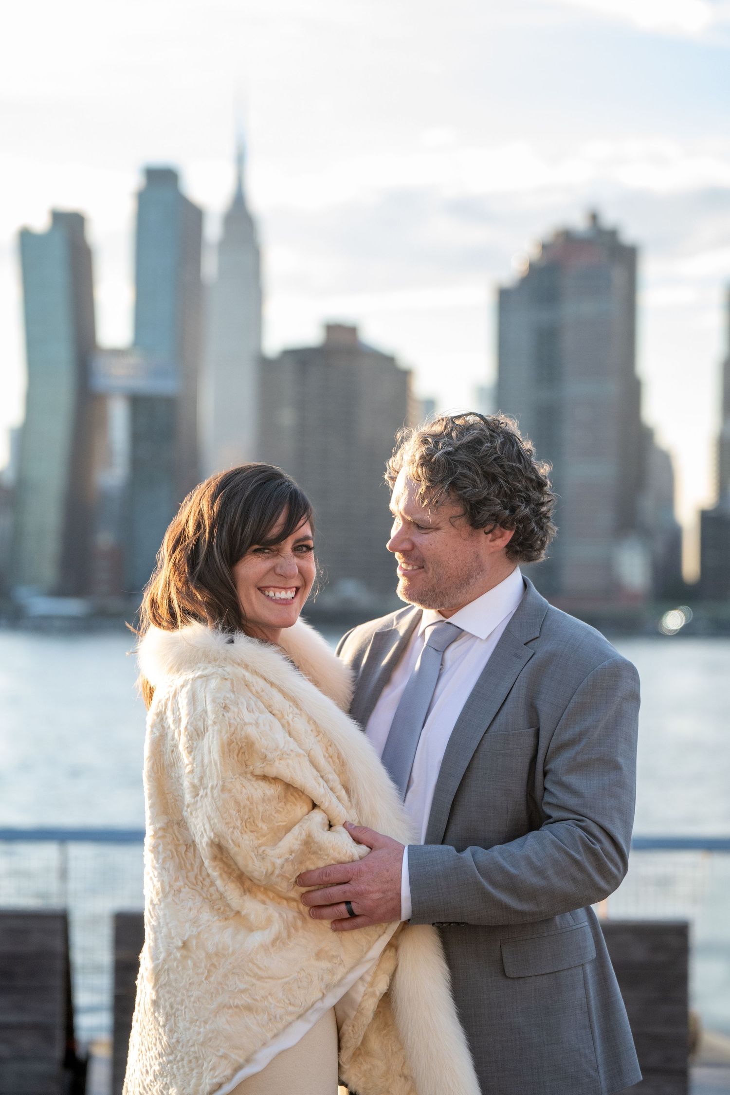 A romantic moment shared between a couple against a waterfront cityscape backdrop.