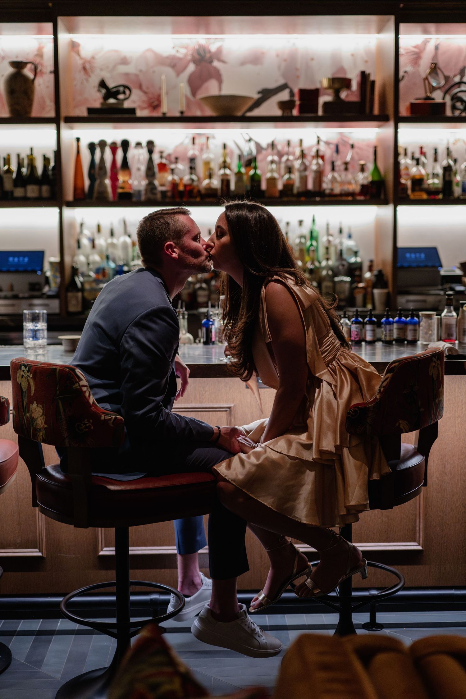 A couple sits at a dimly lit bar sharing an intimate moment in a romantic setting.