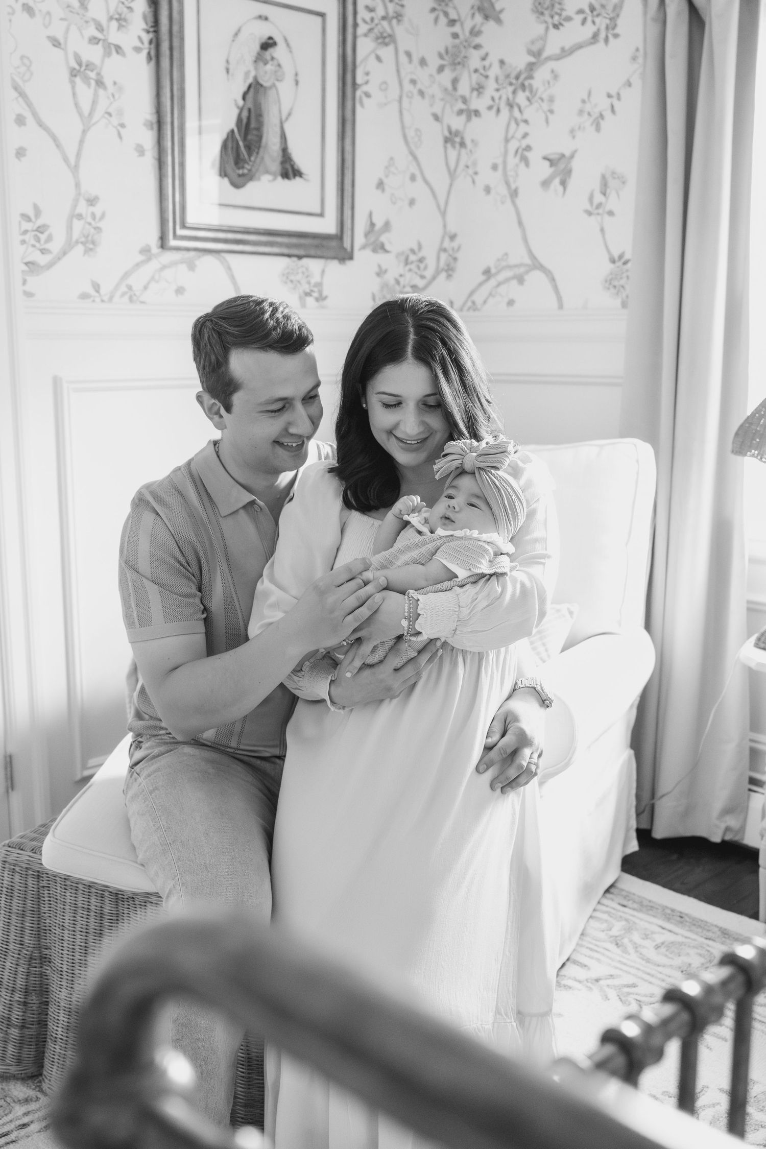 A bright nursery scene with floral wallpaper shows family members sharing intimate moments.