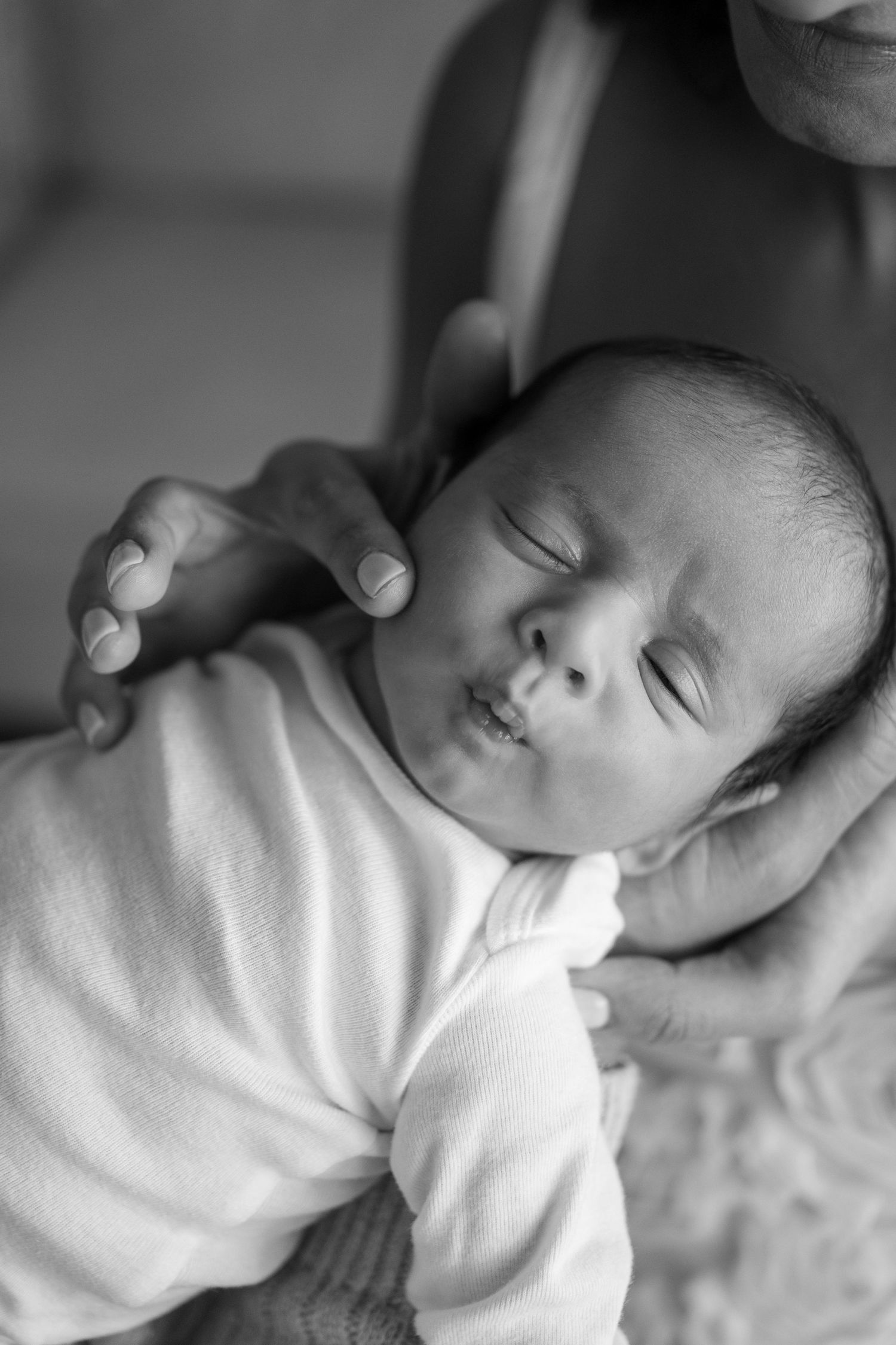 Black and white portrait of peaceful sleeping newborn in white clothing.
