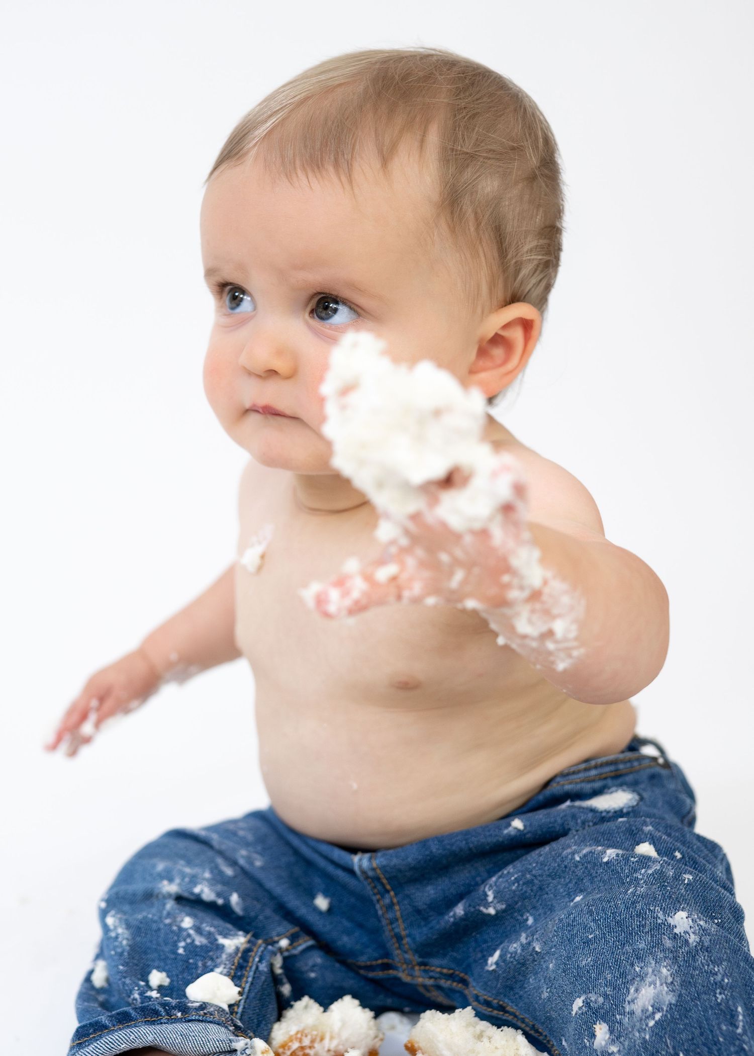 Messy baby with white frosting on hand during first birthday cake smash photo shoot.