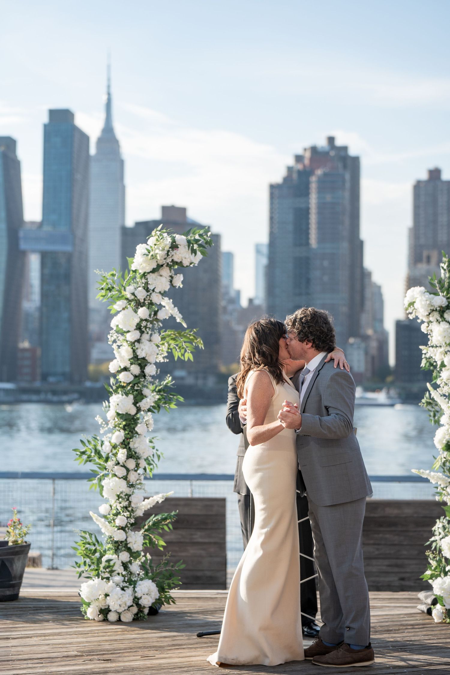 Newlyweds sharing intimate moments under floral arches with NYC skyline backdrop.
