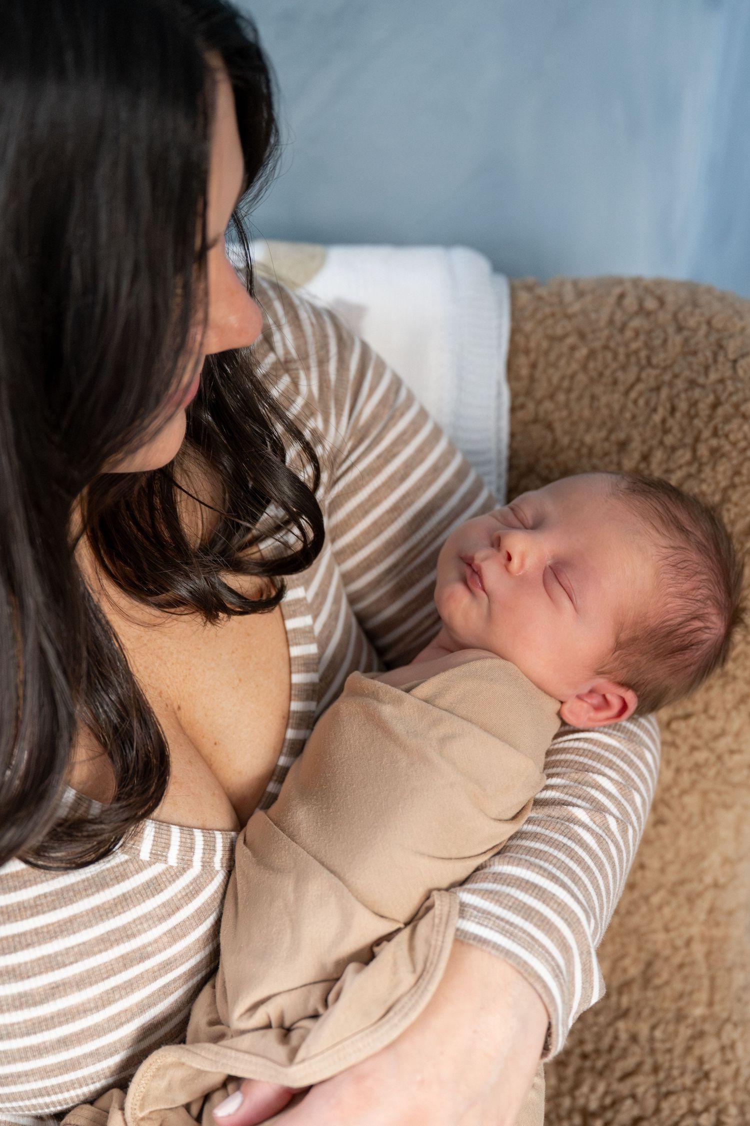 Tender moment between parent and sleeping infant in matching striped outfits.