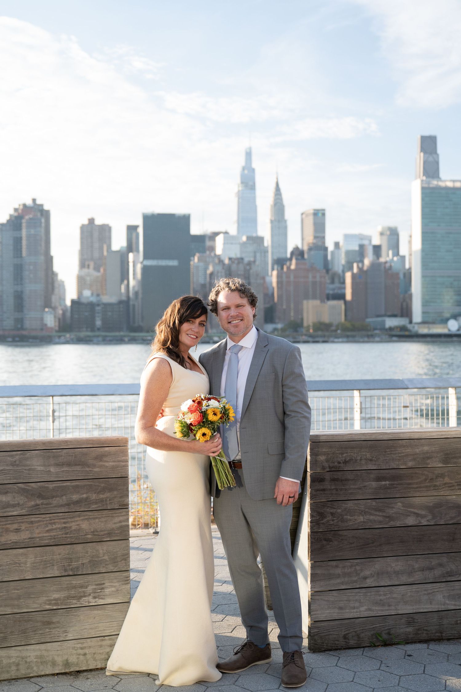 Wedding couple poses along waterfront deck with Manhattan skyline view at Gantry Plaza State Park in Long Island City.