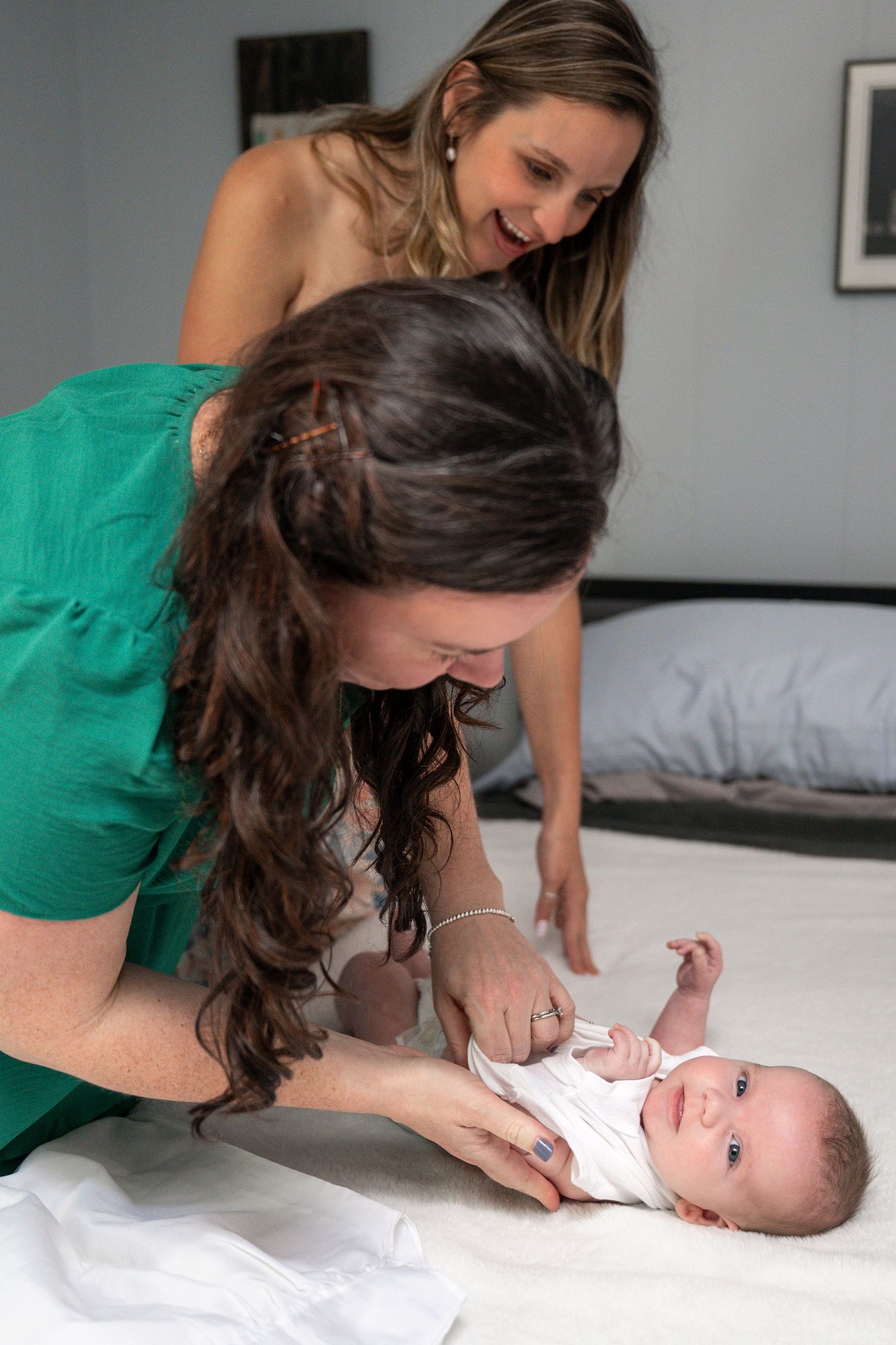 A tender moment captured as a caregiver in green interacts with a baby on white bedding.