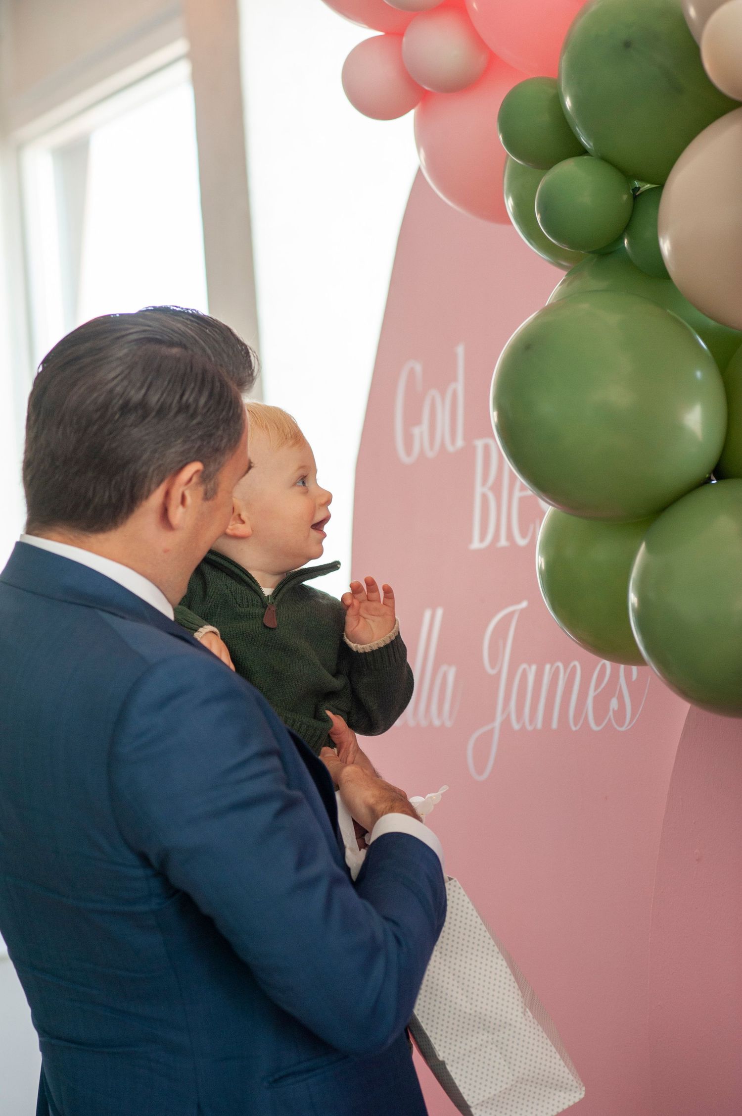 Pink and green balloon arch decorates a wall at a celebration event.