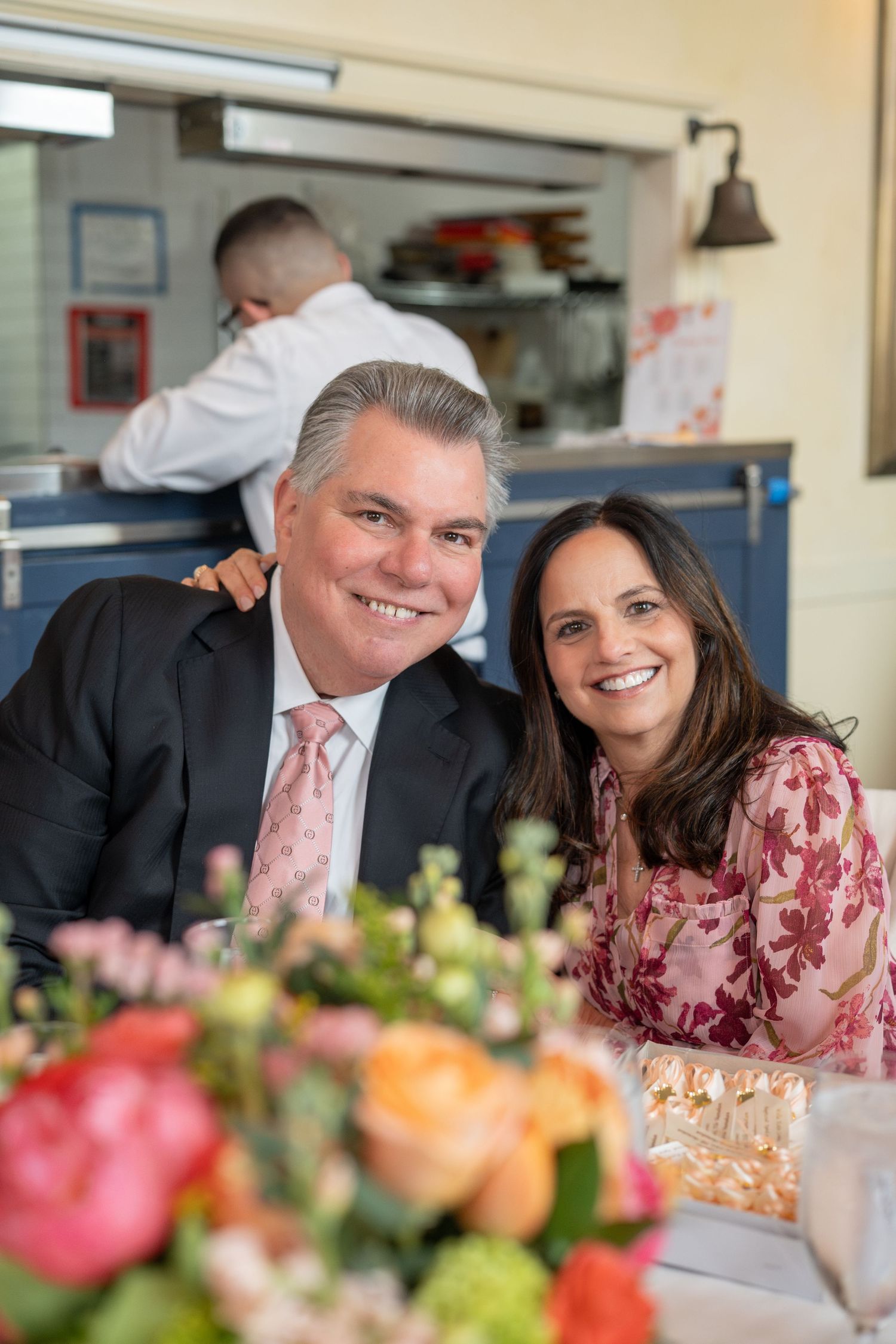 Smiling couple posing together at a christening reception with floral centerpiece.