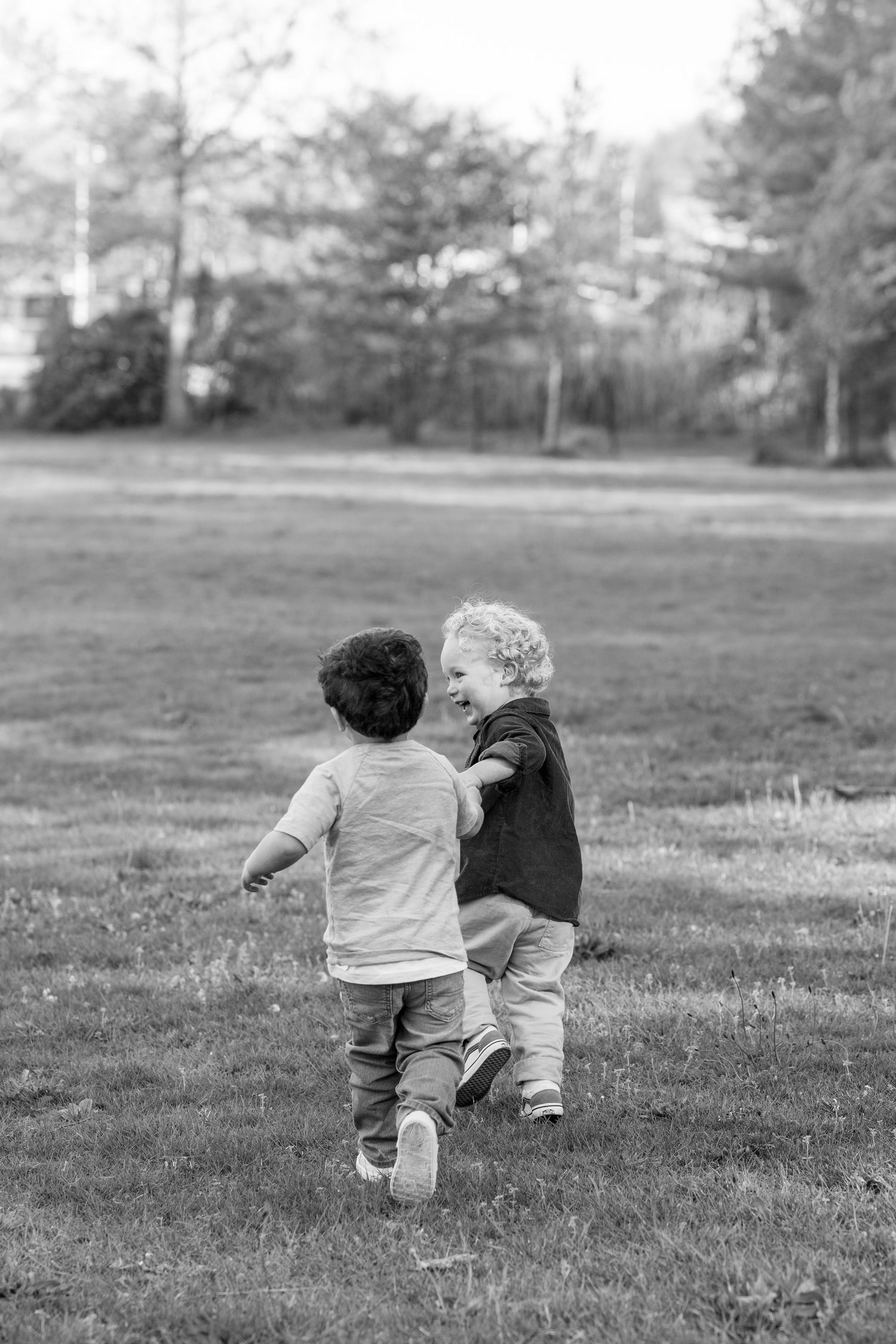 Black and white photo of two young boys running and playing together in a grassy park.