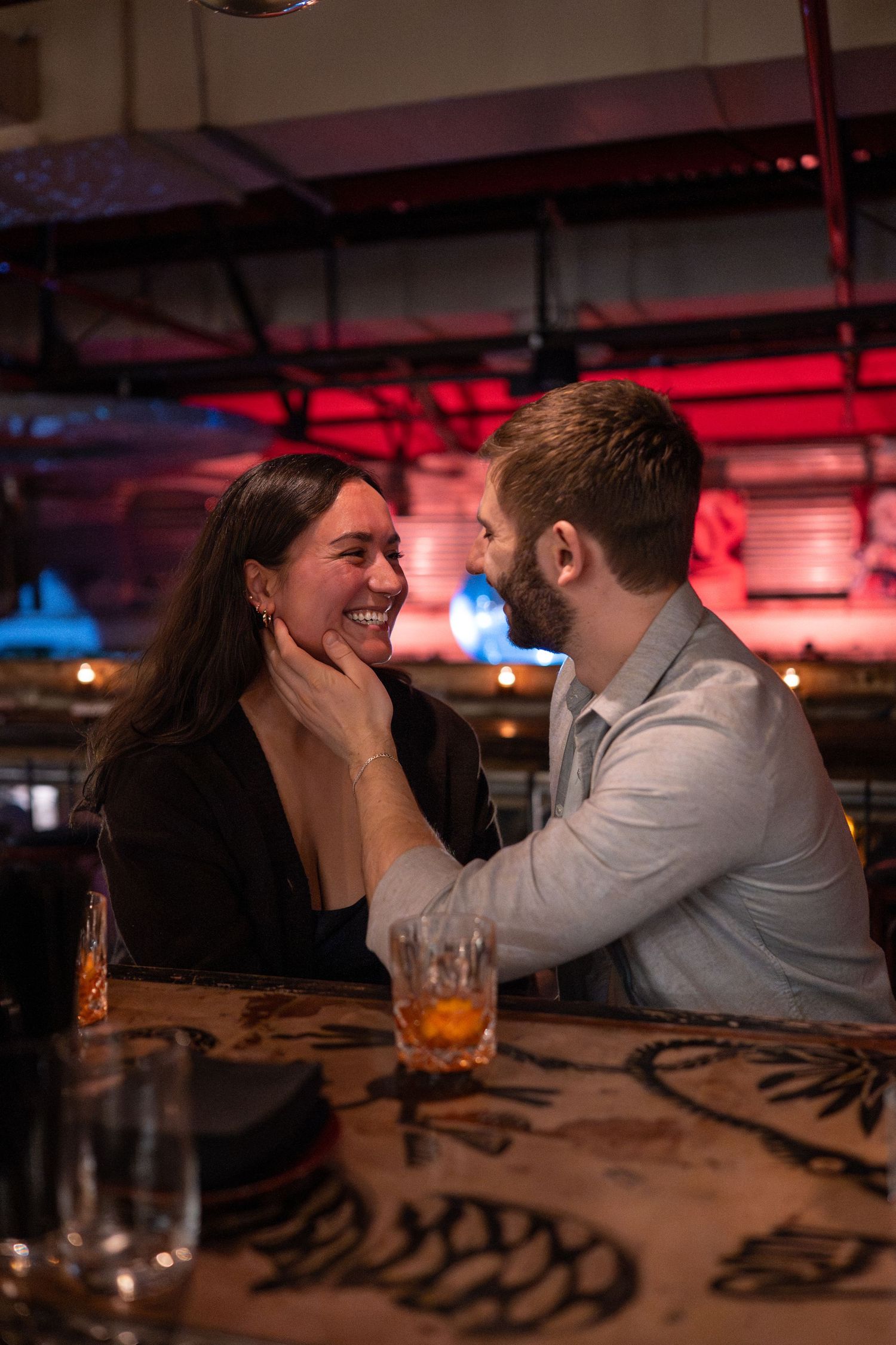 A couple shares an intimate moment at a dimly lit bar with red ambient lighting.