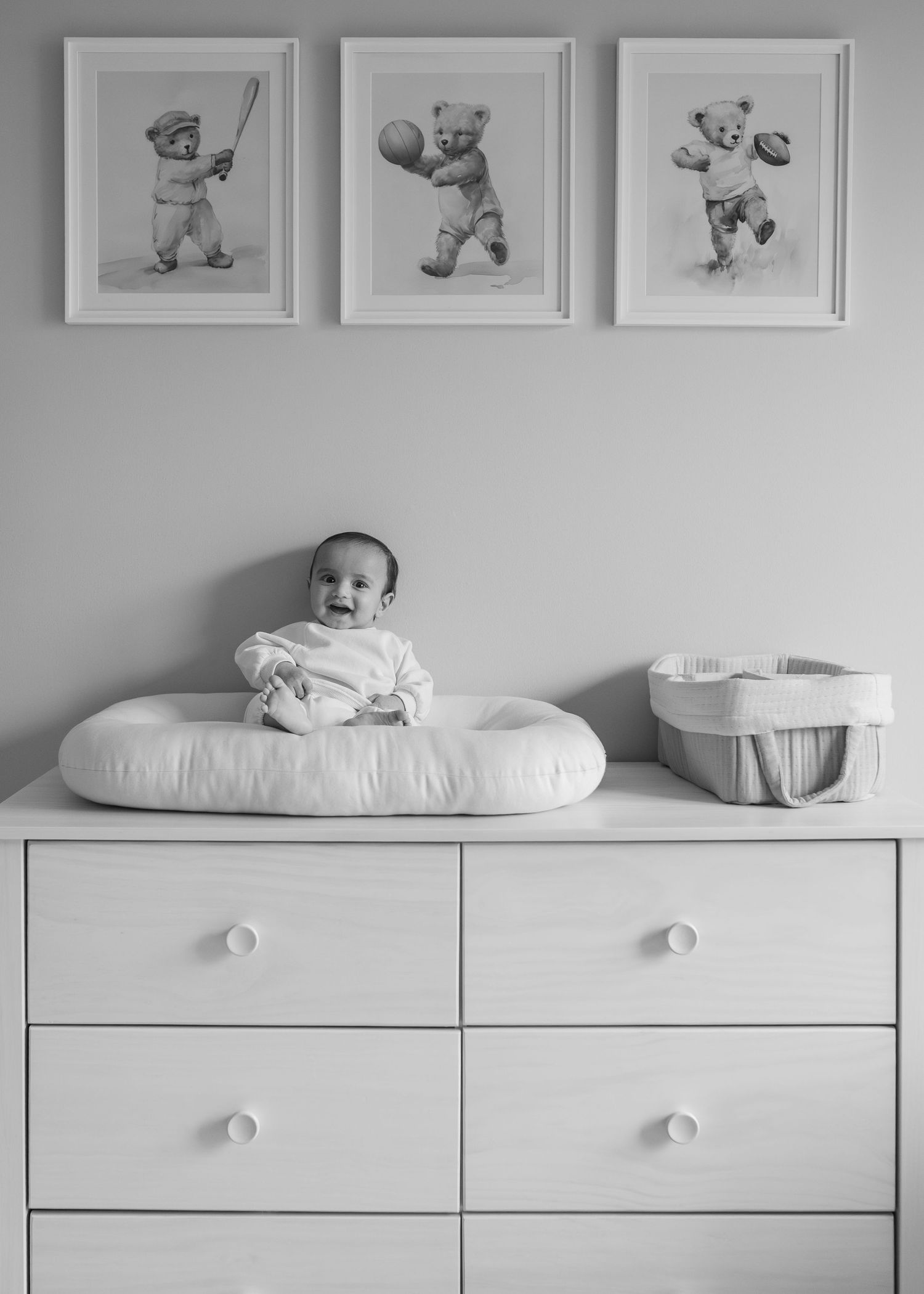 A minimalist nursery interior with white furniture and framed artwork featuring teddy bears mounted on a gray wall.
