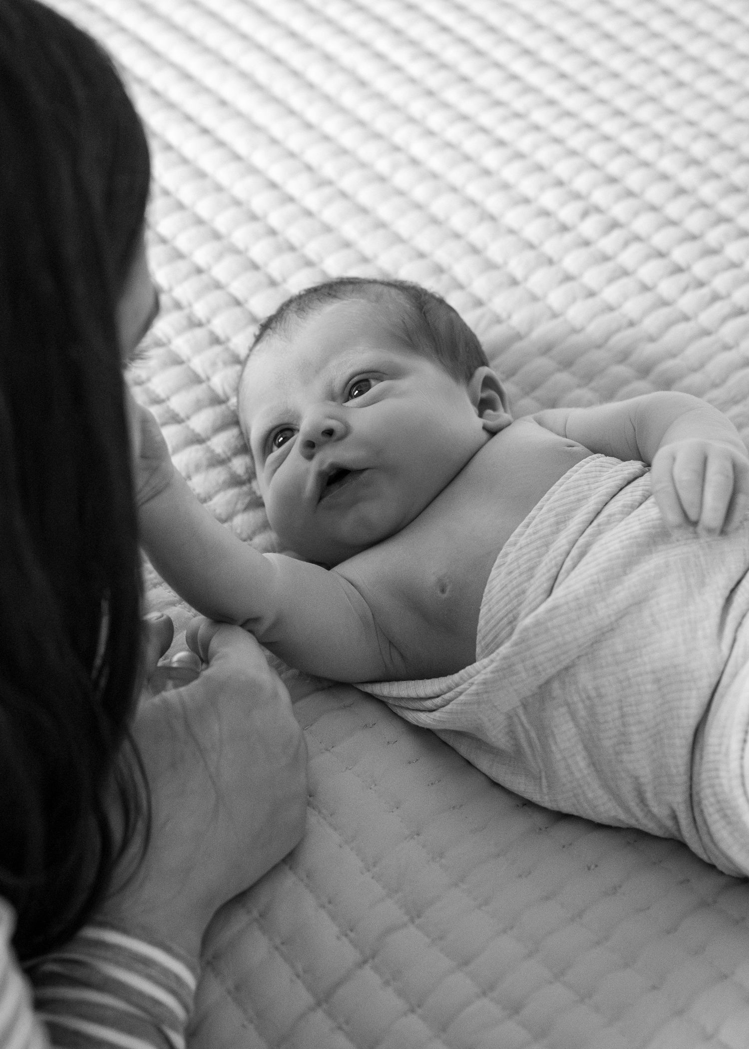 Close-up view of a newborn baby lying on a quilted white surface.