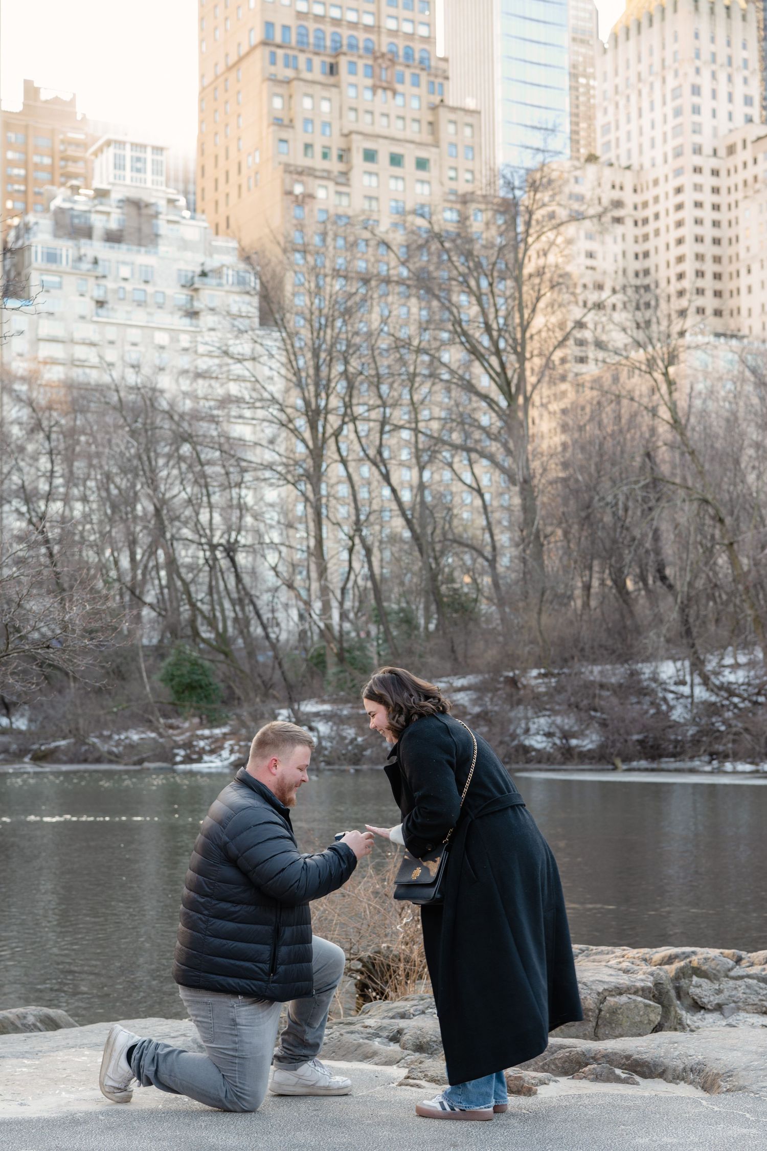 A proposal sequence showing two people kneeling by a lake in Central Park with city buildings in the background.