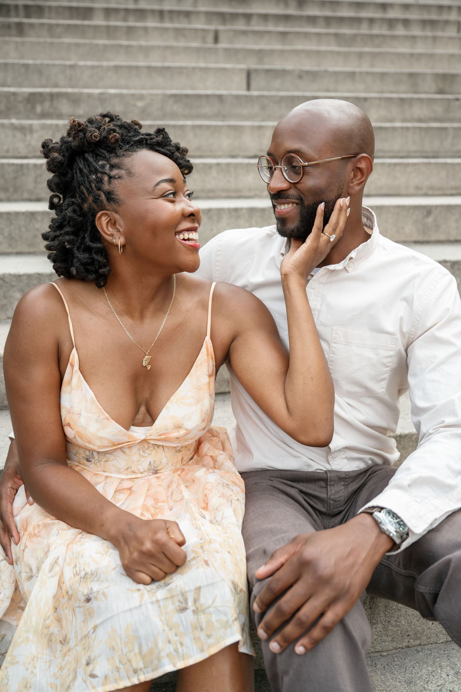A couple sits on stone steps sharing joyful laughter and intimate moments in a romantic engagement photoshoot series.