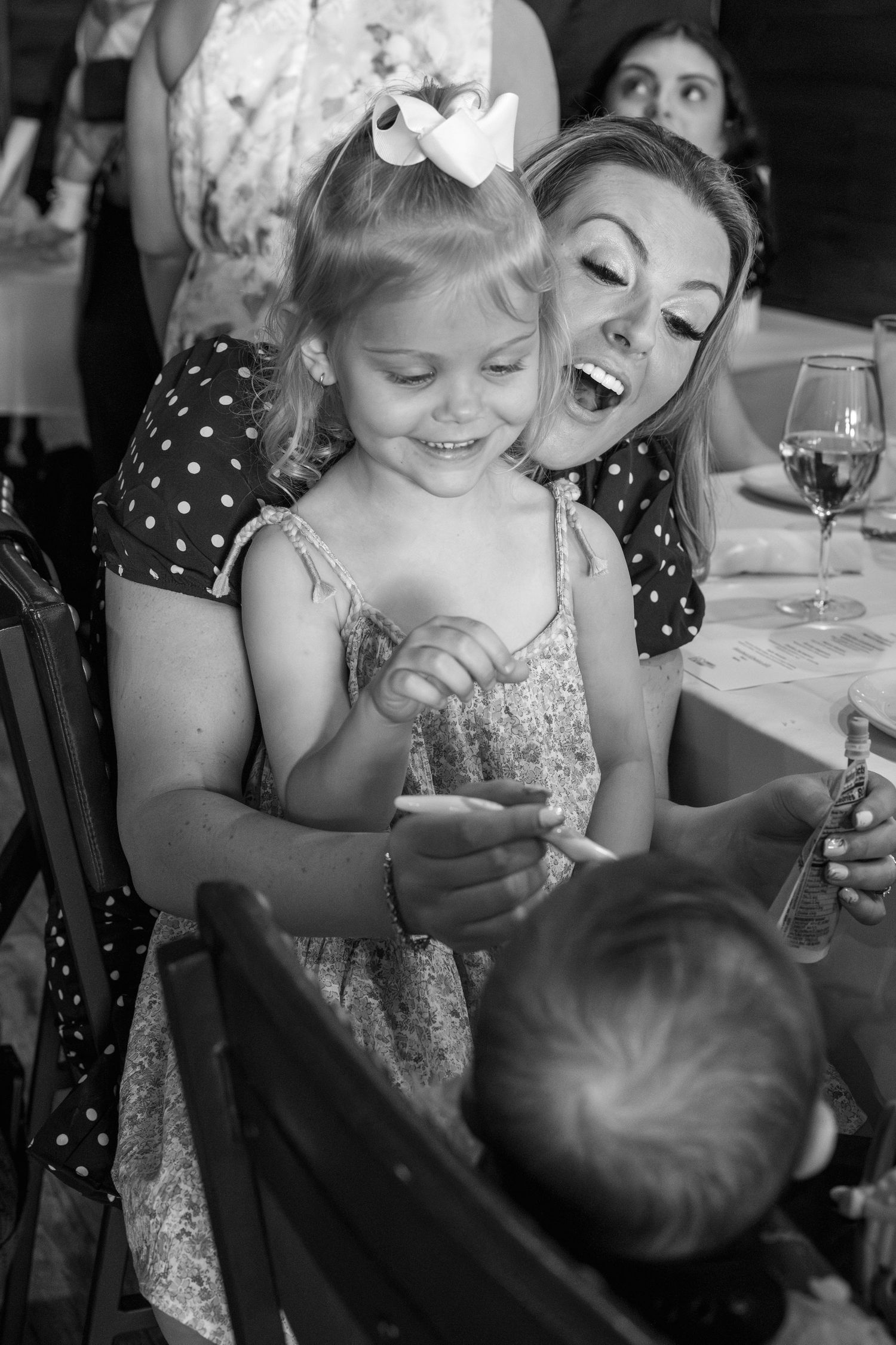 A black and white photo captures joyful laughter between adults and a young child wearing a crown.