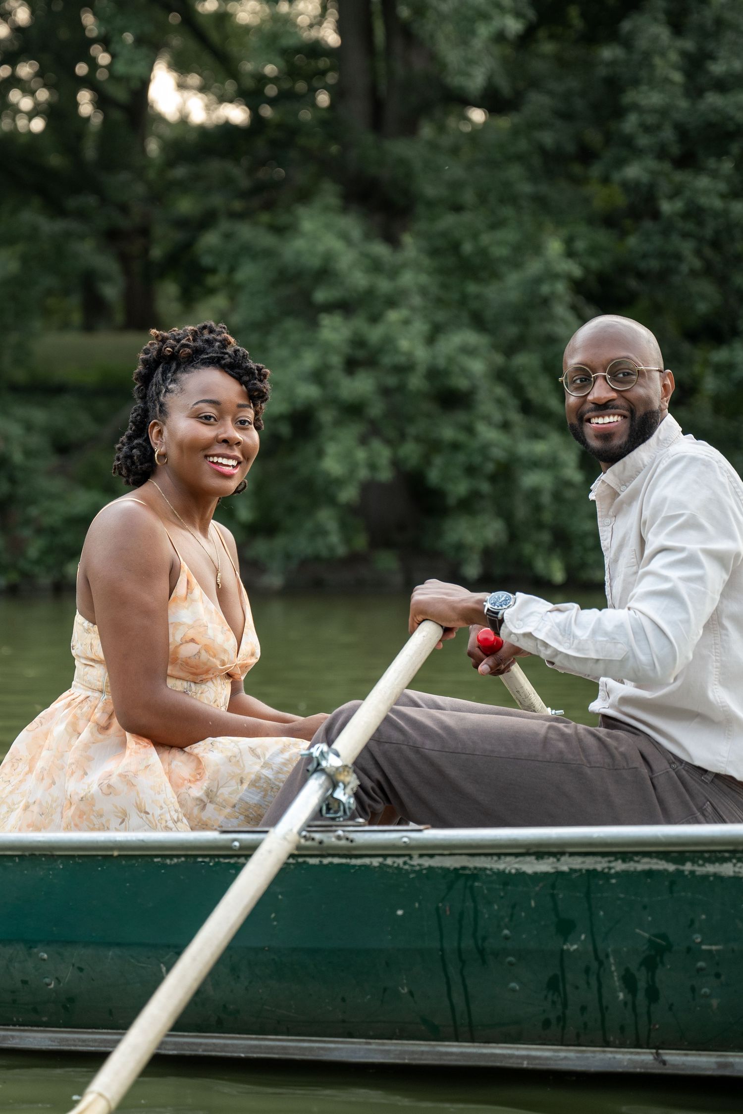 A happy couple enjoys a boat ride together on a lake surrounded by lush greenery.