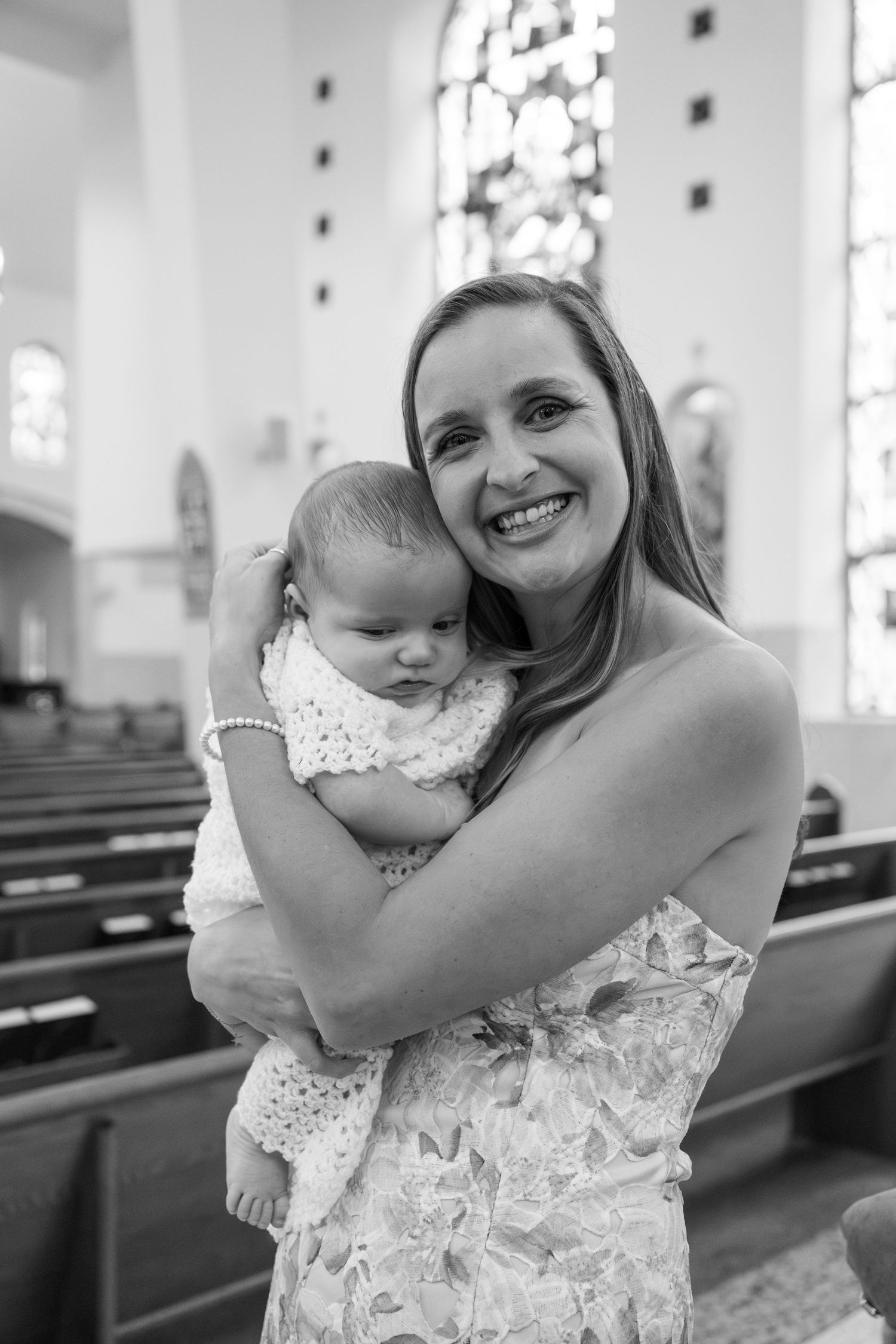 A tender moment captured in black and white inside a church with stained glass windows in the background.