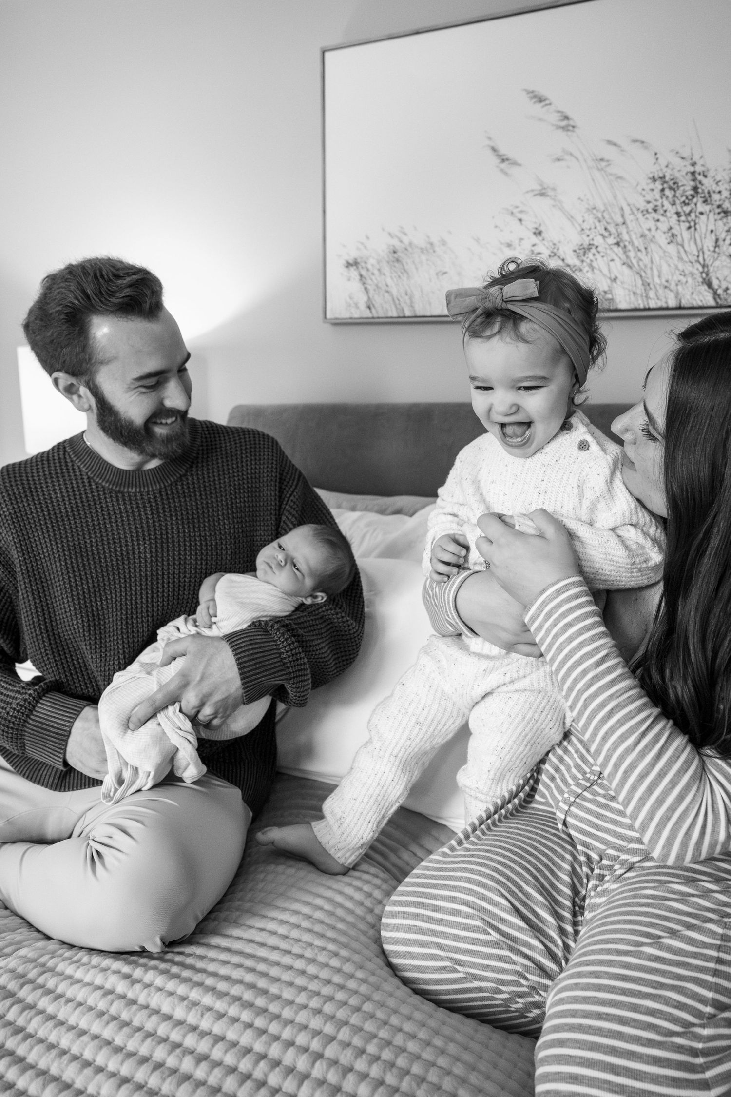 Black and white photos showing joyful family interactions on a striped bedspread.