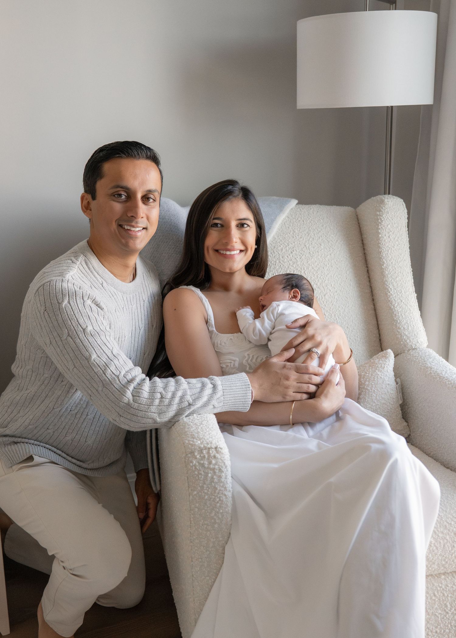 Parents lounging on white couch with newborn in bright modern room.