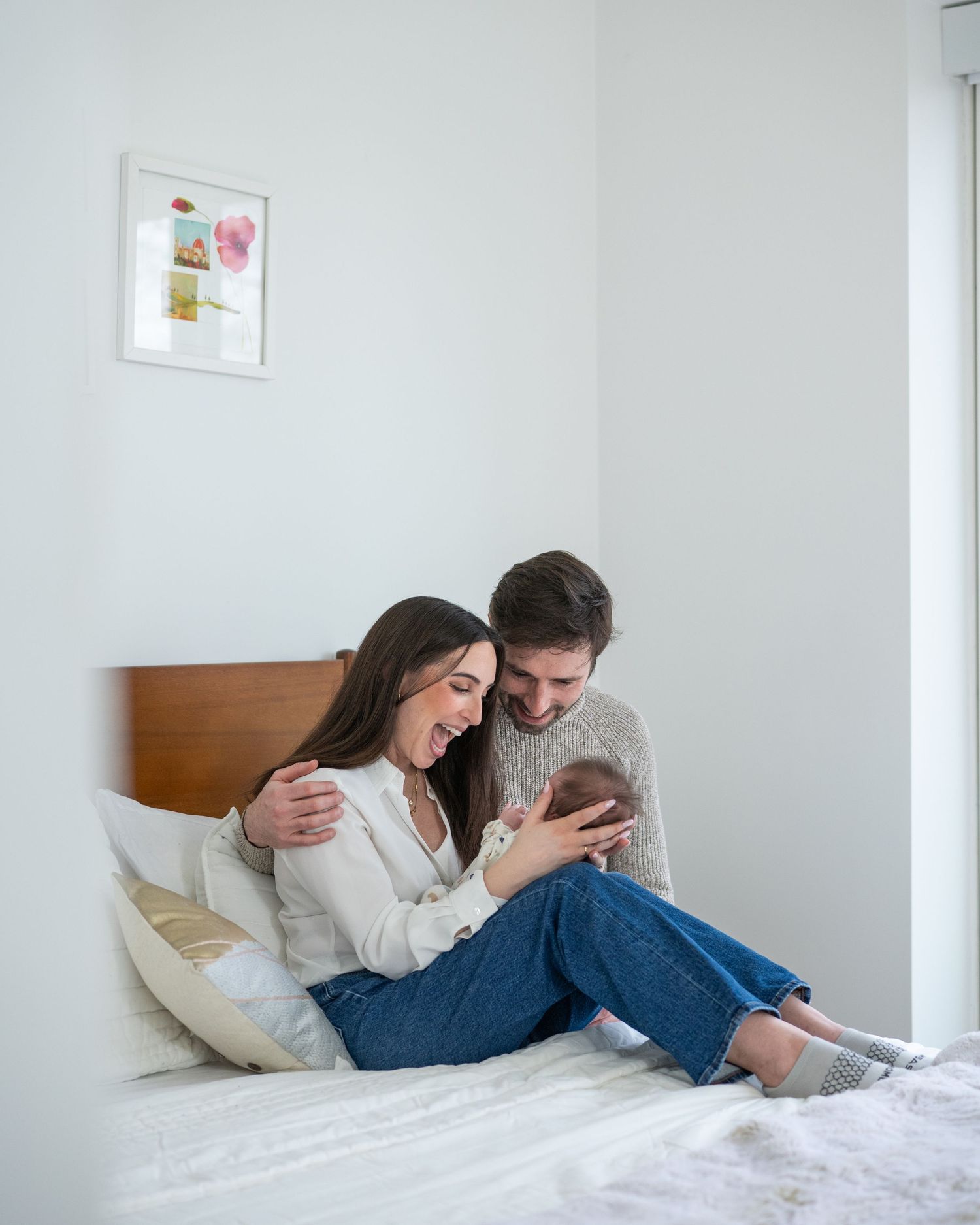 Family sharing intimate moments together on a white bed with wall art in background.