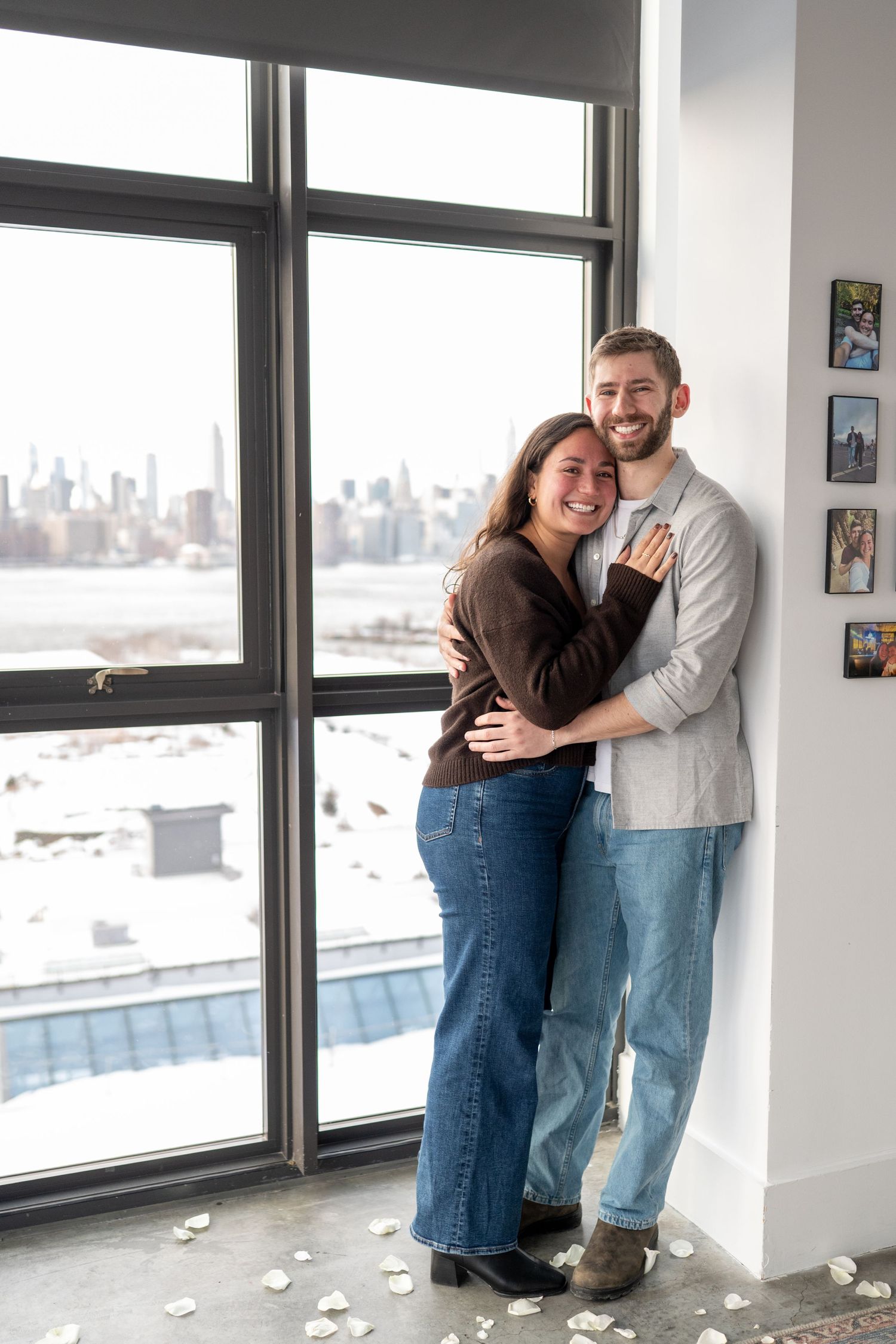 A couple shares a joyful moment by large windows overlooking a cityscape in a bright modern interior space.