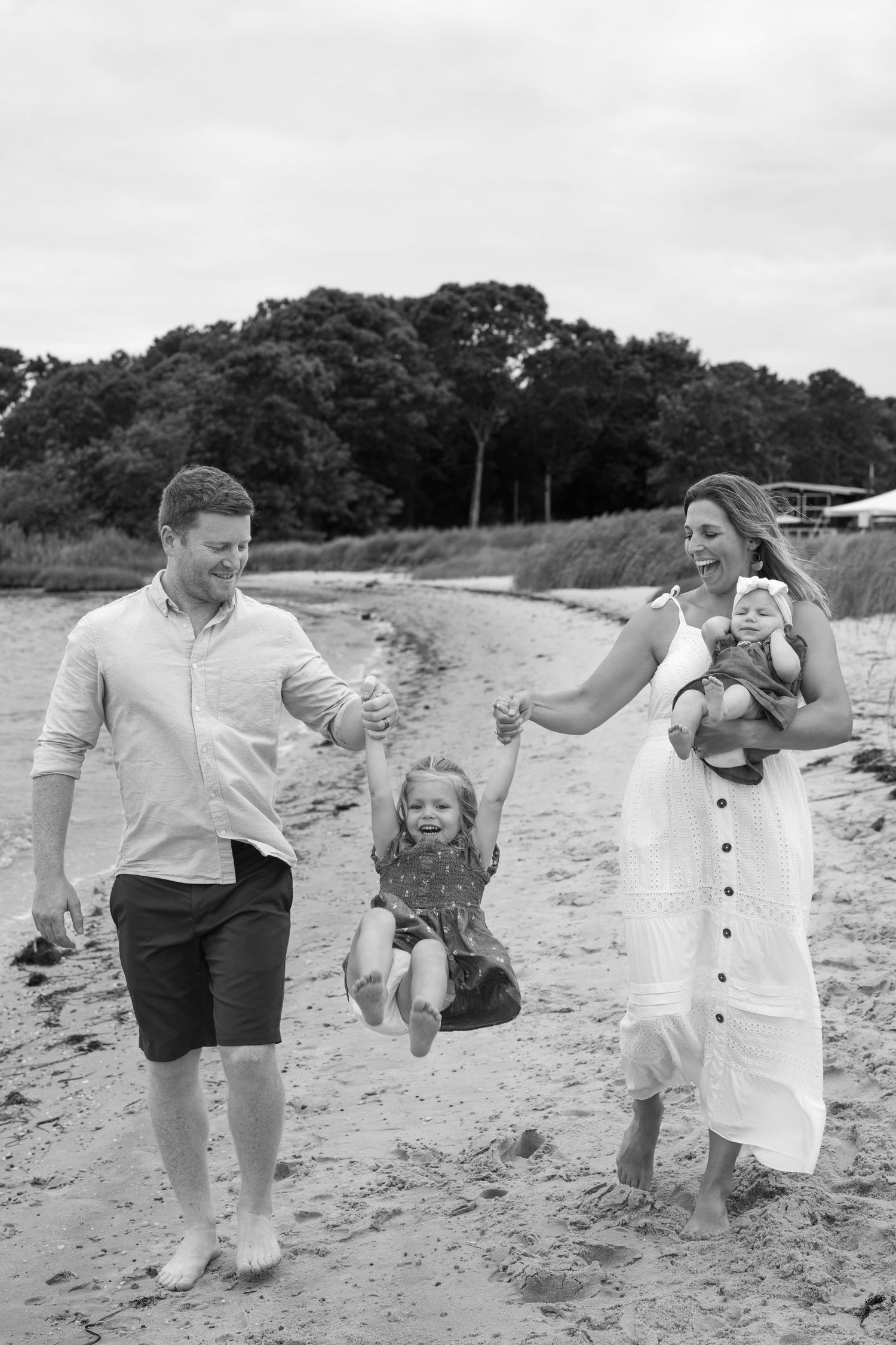 Family playing and swinging child while walking along a beach shoreline.