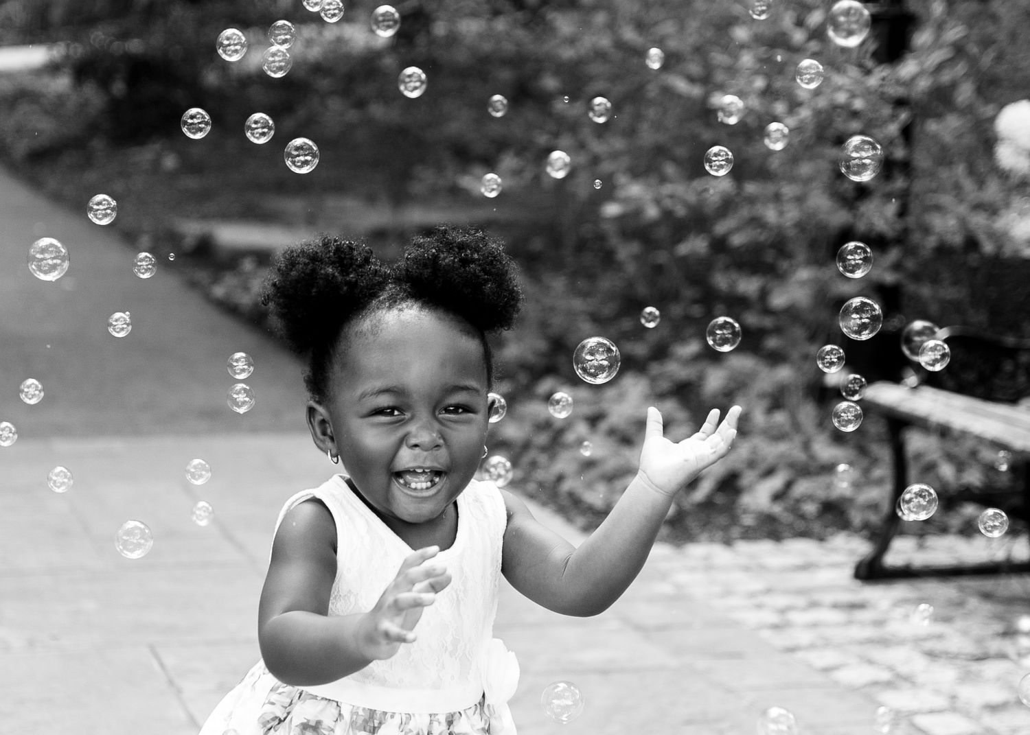 Child plays with bubbles outdoors in black and white photography.