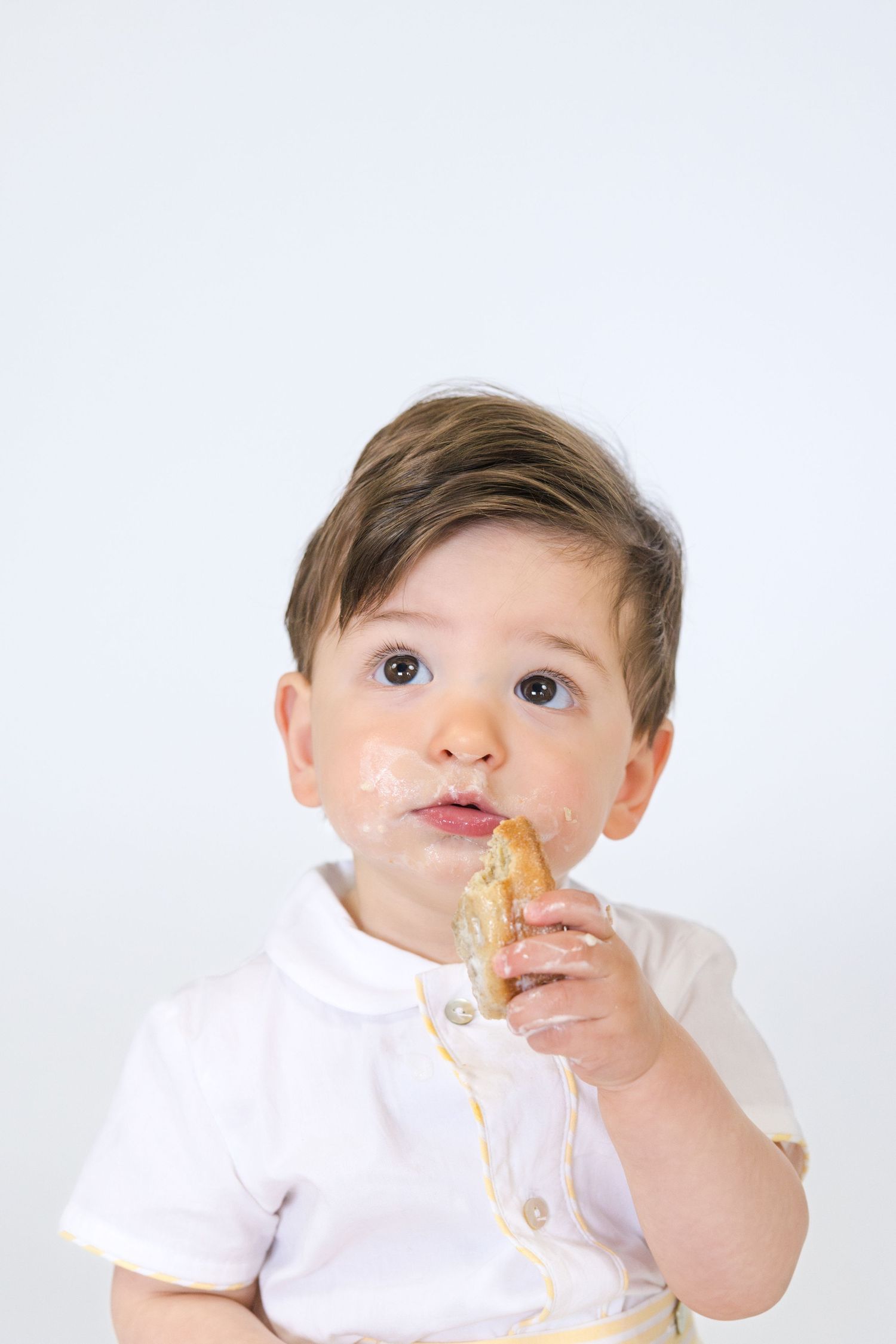 Baby in white outfit enjoys birthday cake smash.