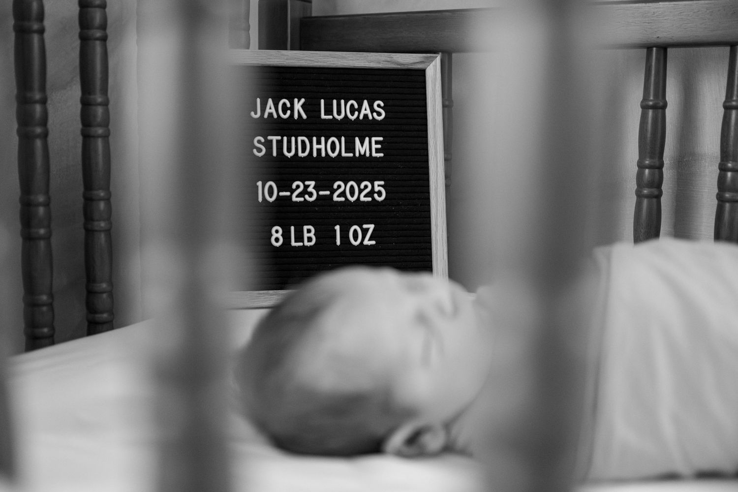 Black and white hospital birth record card showing name, date, and weight details against a blurred background.