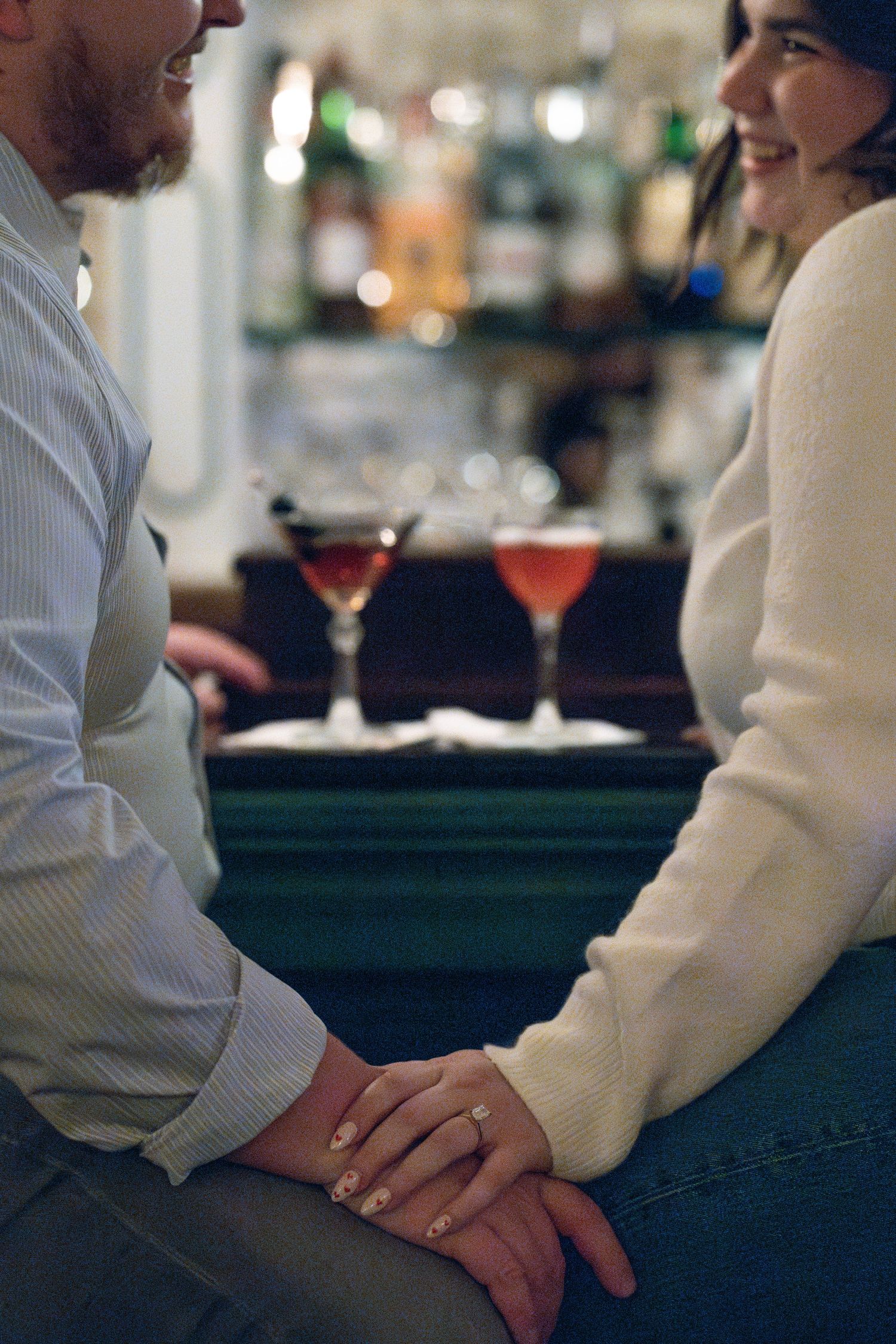 A couple holds hands across a bar counter while having an intimate conversation.