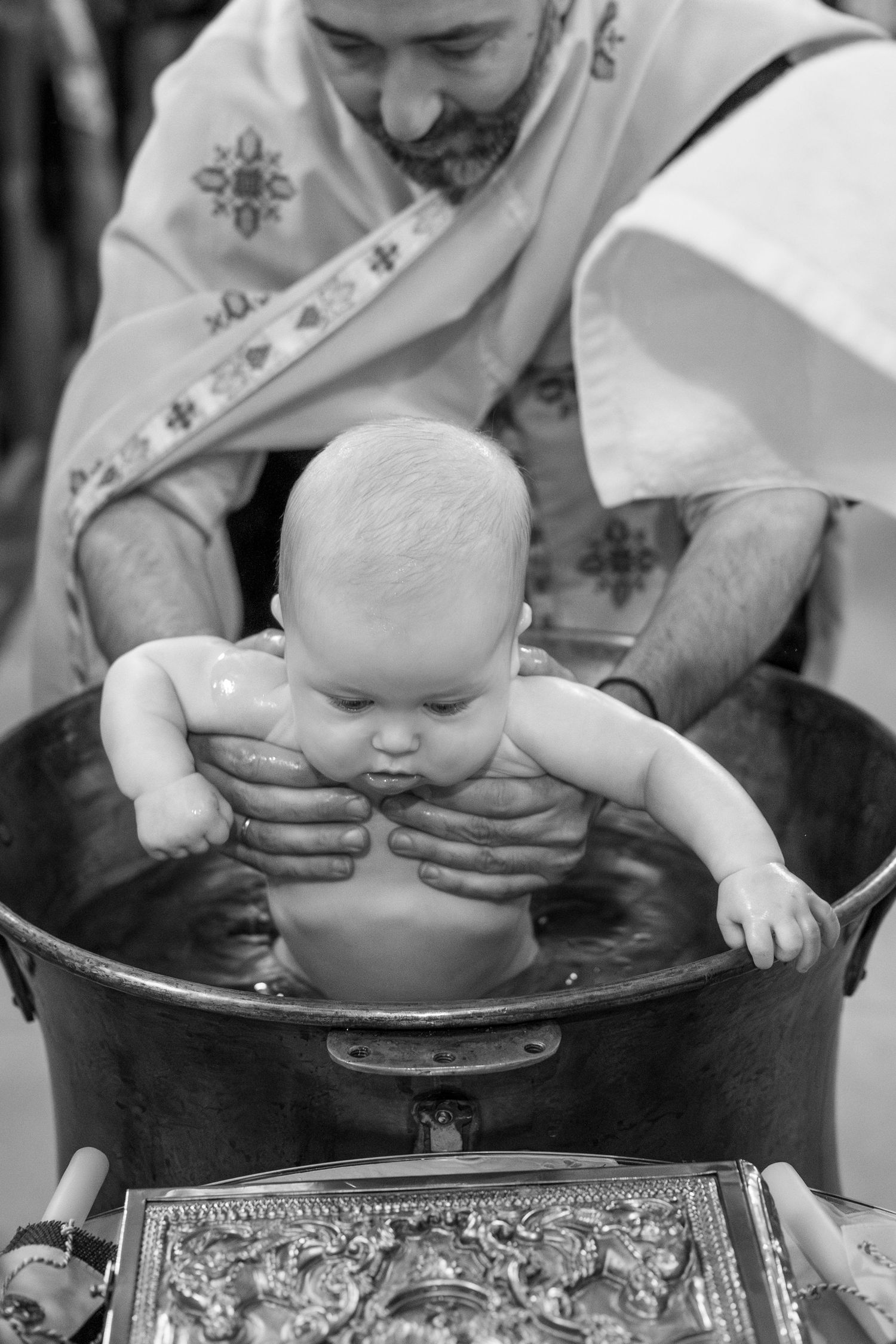 A sequence of black and white photos showing a baby being baptized in a traditional religious ceremony.