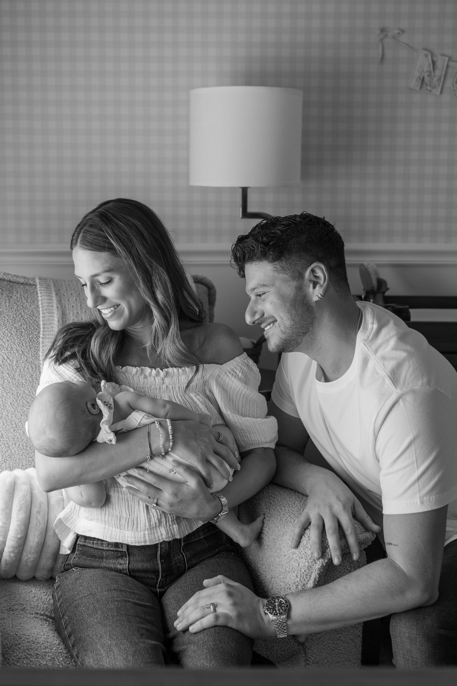 Family lounges together on grey couch sharing intimate moments in black and white photography.