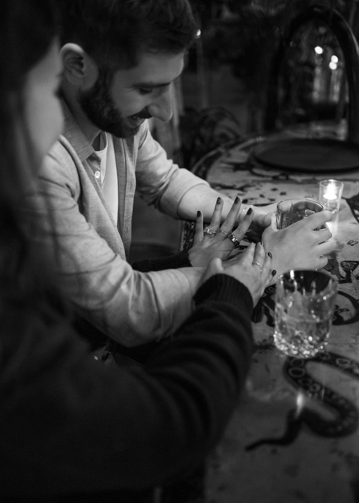 A romantic black and white candlelit moment between a couple holding hands across a table.