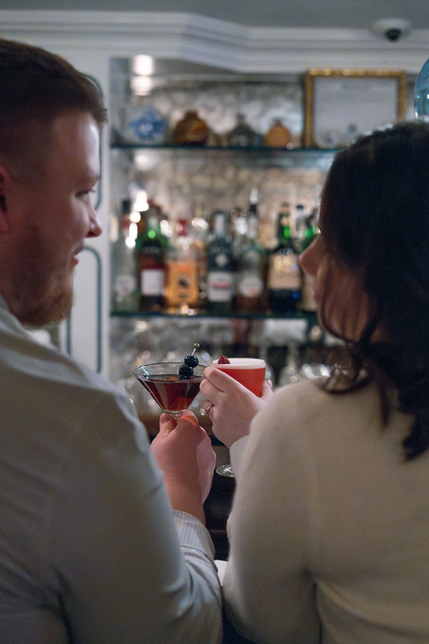 Two people enjoying cocktails together at an elegant bar with bottles displayed in the background.