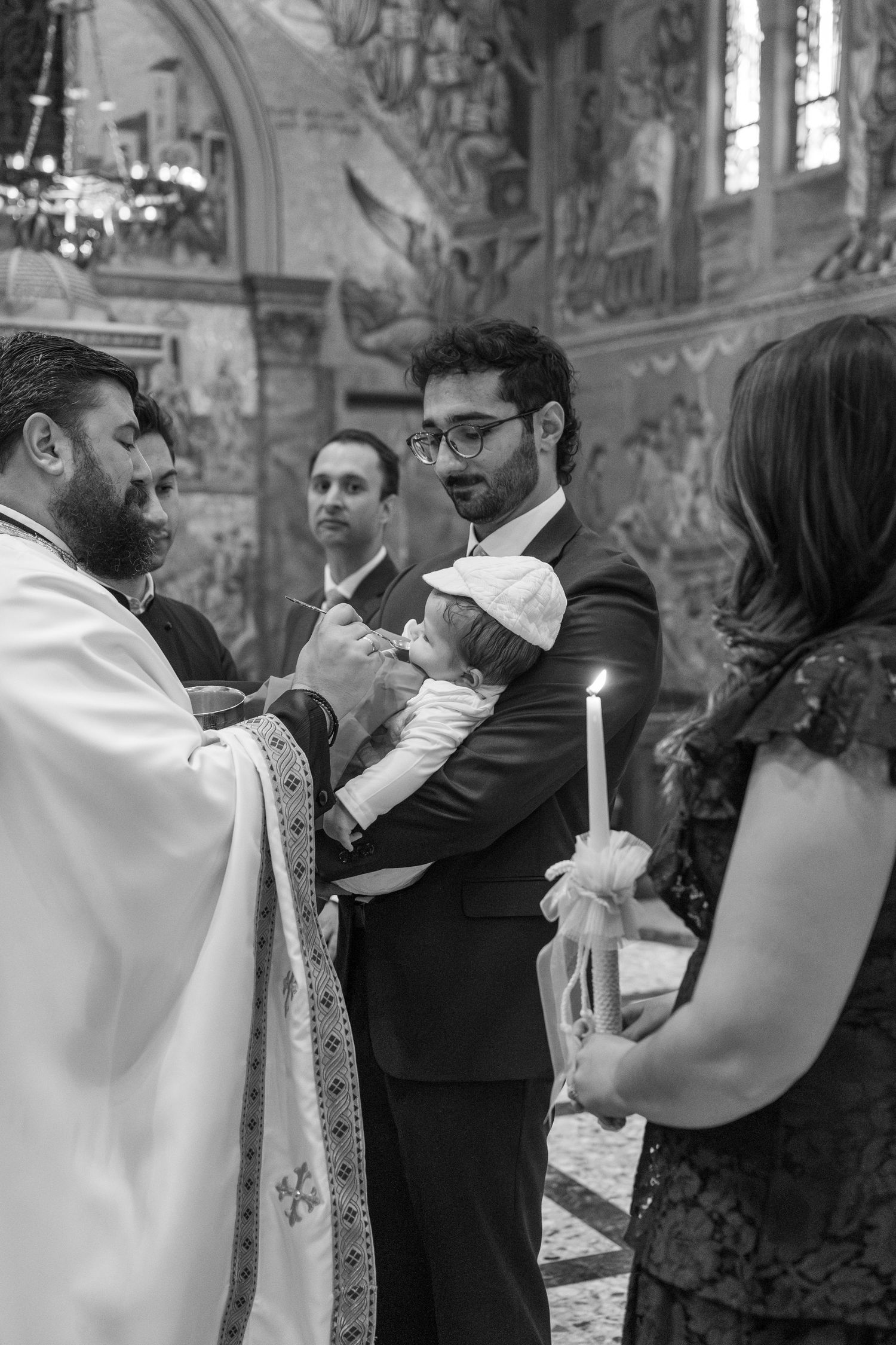 A religious ceremony in progress inside a church with ornate wall paintings and candles.
