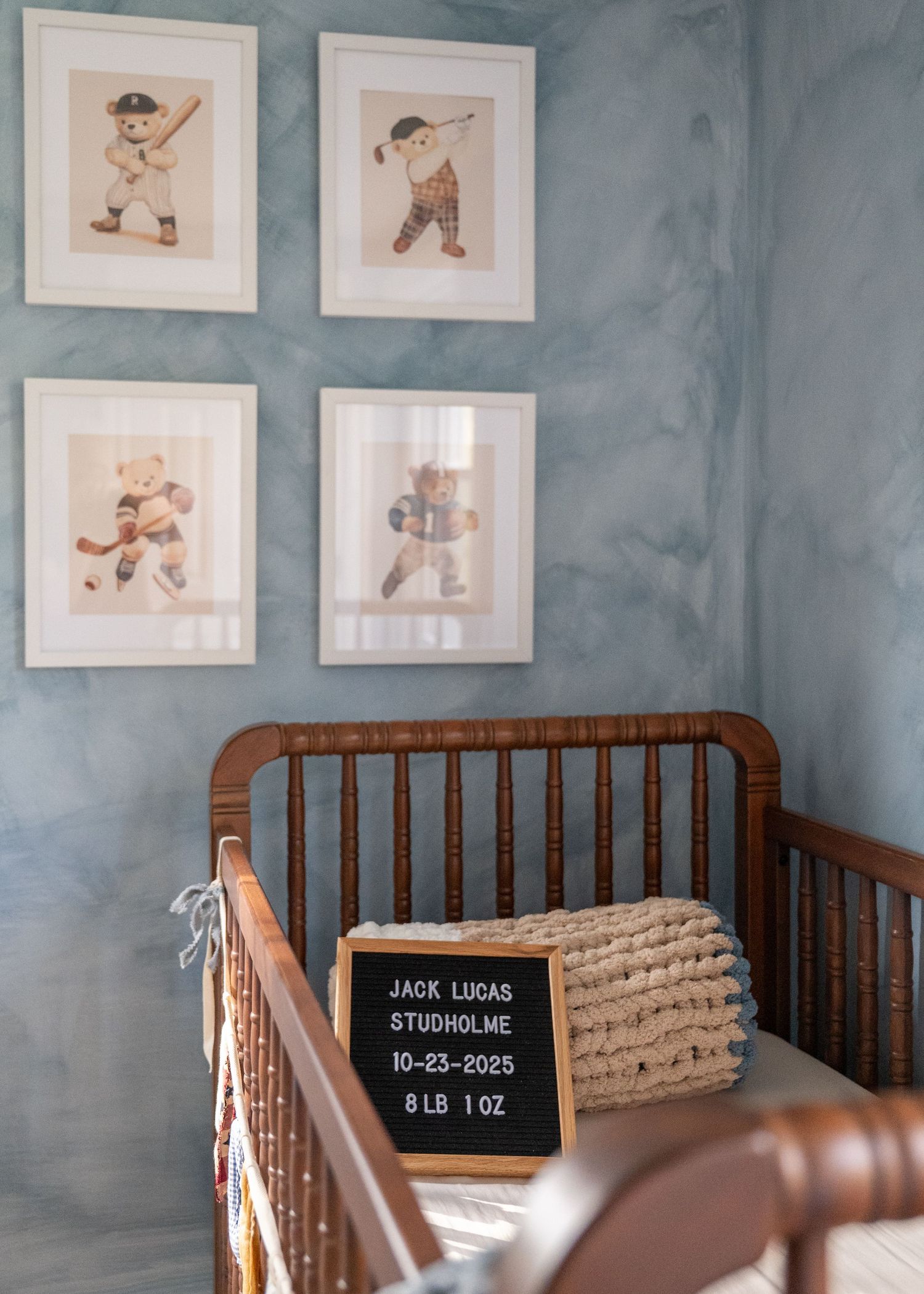 A nursery room with dark wooden cribs and framed artwork of children playing displayed on blue-gray walls.