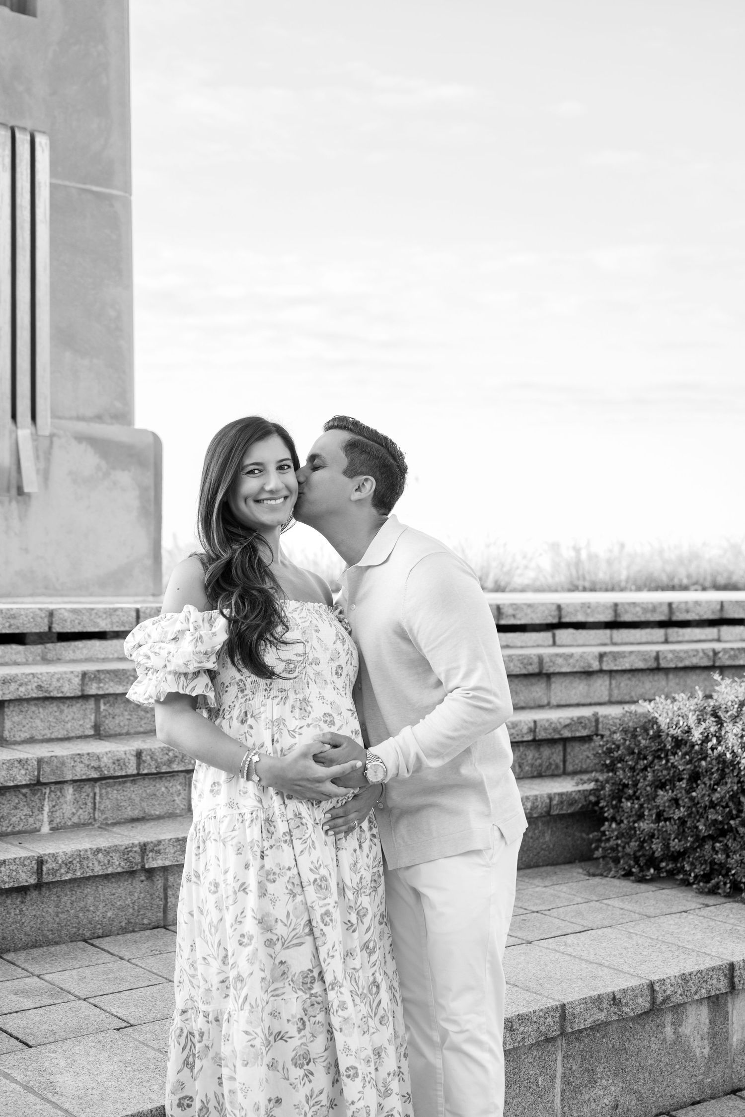 A couple shares a romantic moment on stone steps in black and white photography.