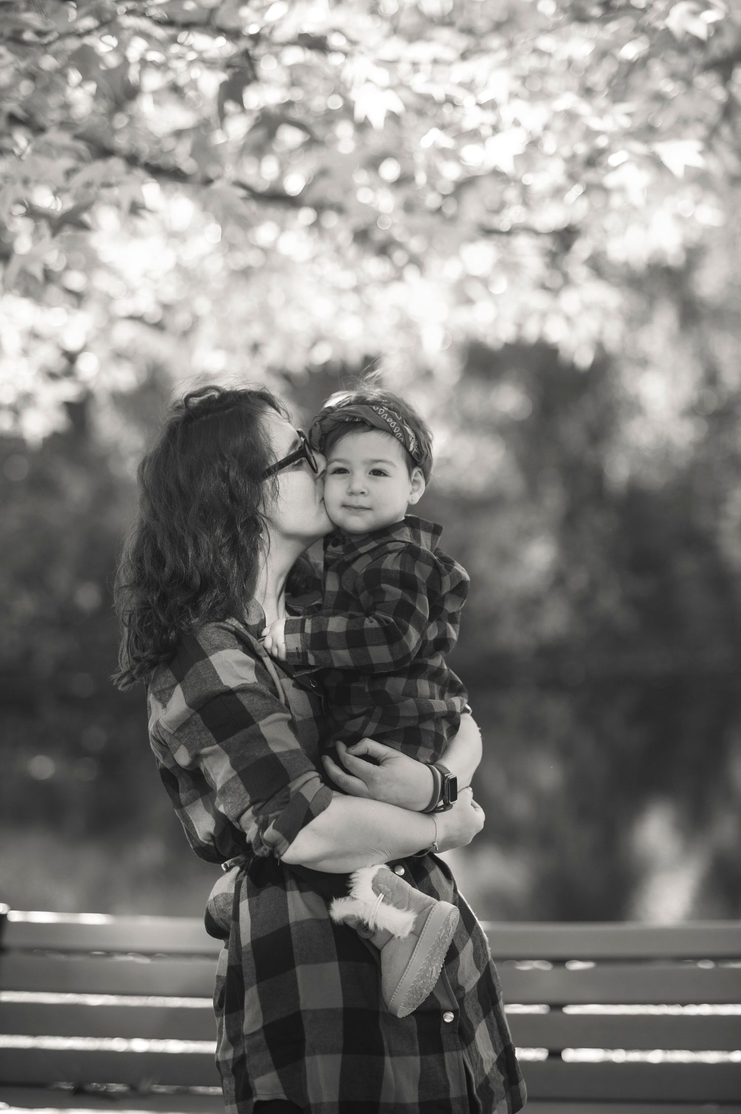 A tender black and white portrait of two people in plaid sharing an affectionate moment on a park bench.