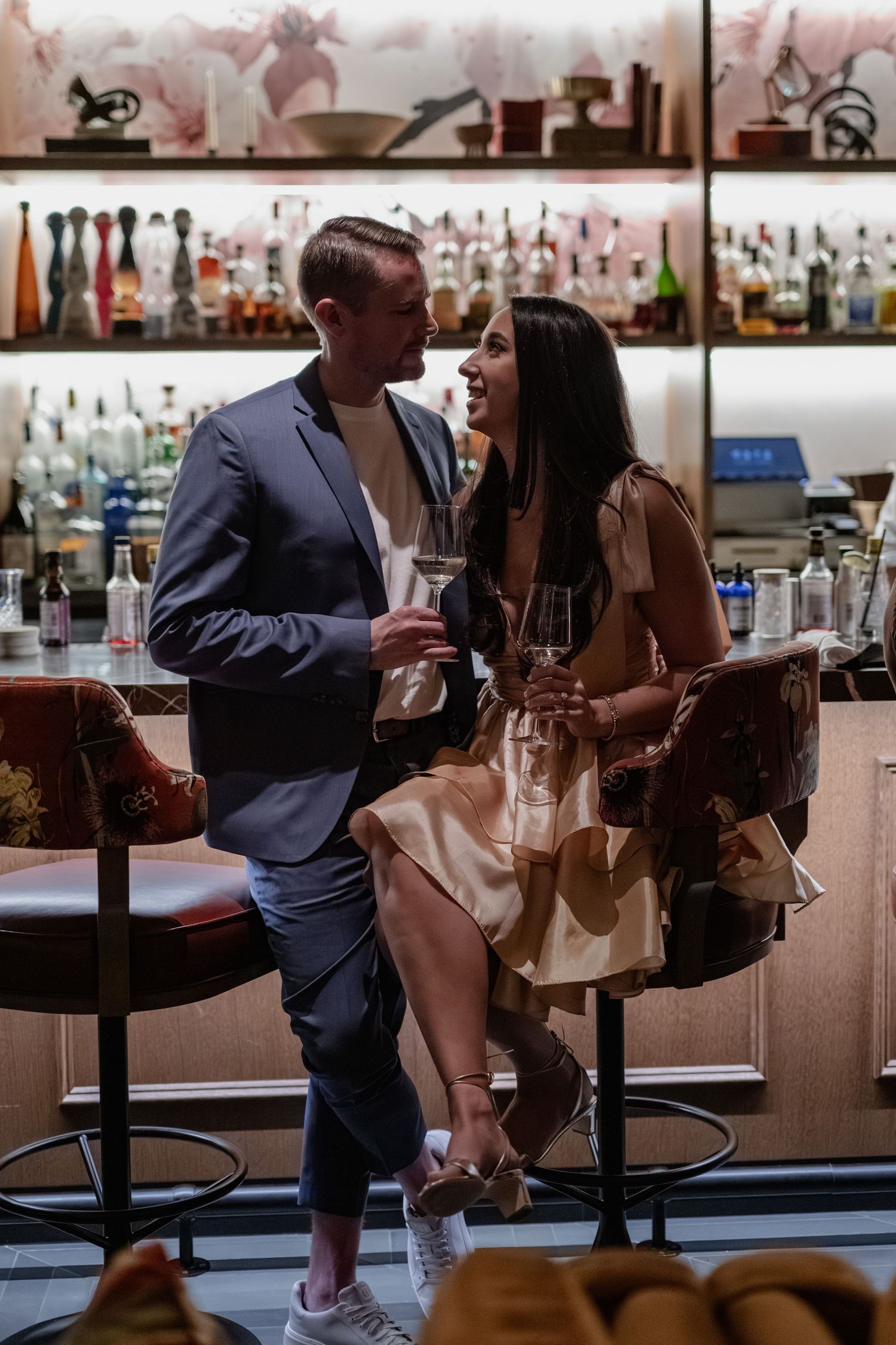 Couple enjoying drinks together at an upscale bar with bottles displayed in the background.
