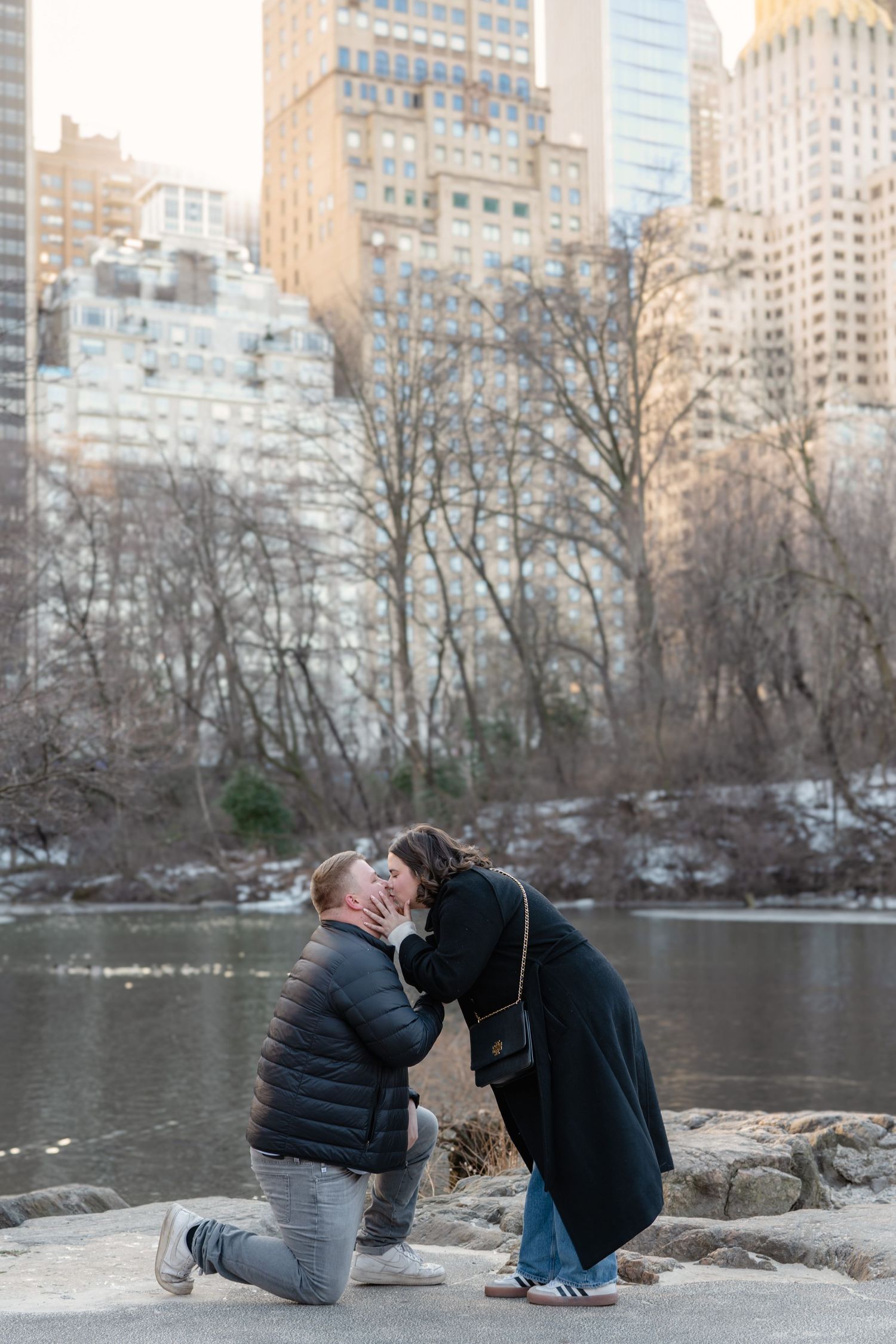 Couple getting engaged in front of a winter cityscape with snow-covered trees and buildings.