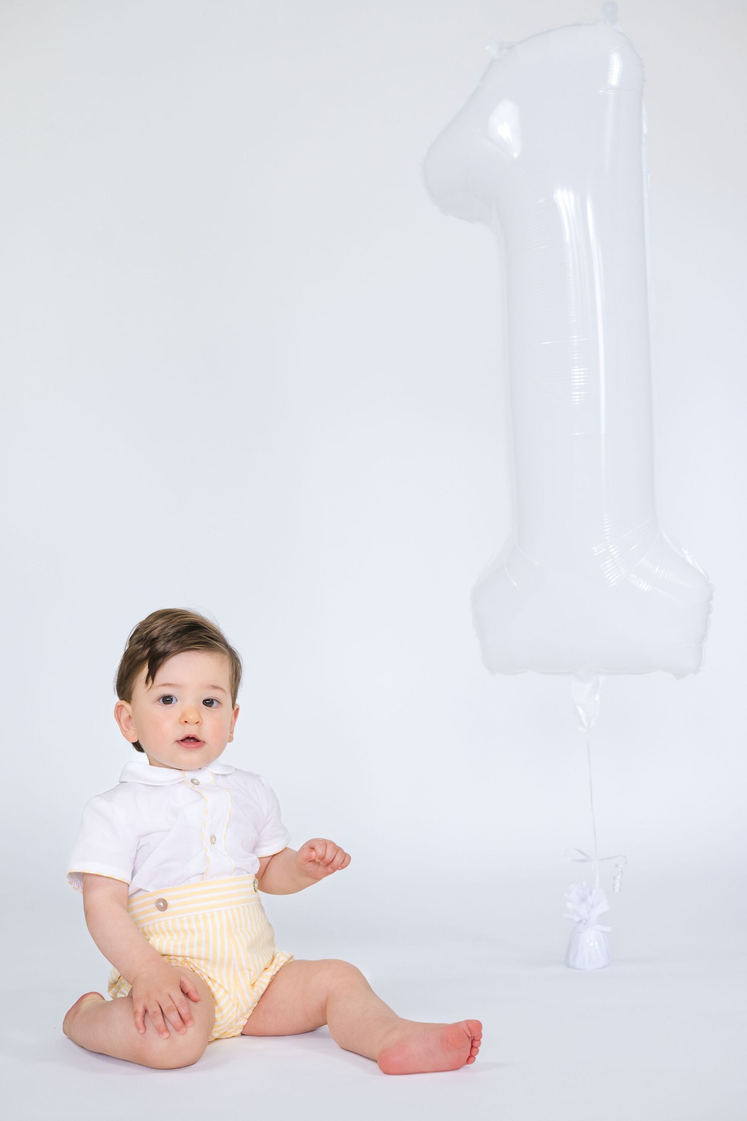 Baby in white outfit sitting on white background with playful poses.