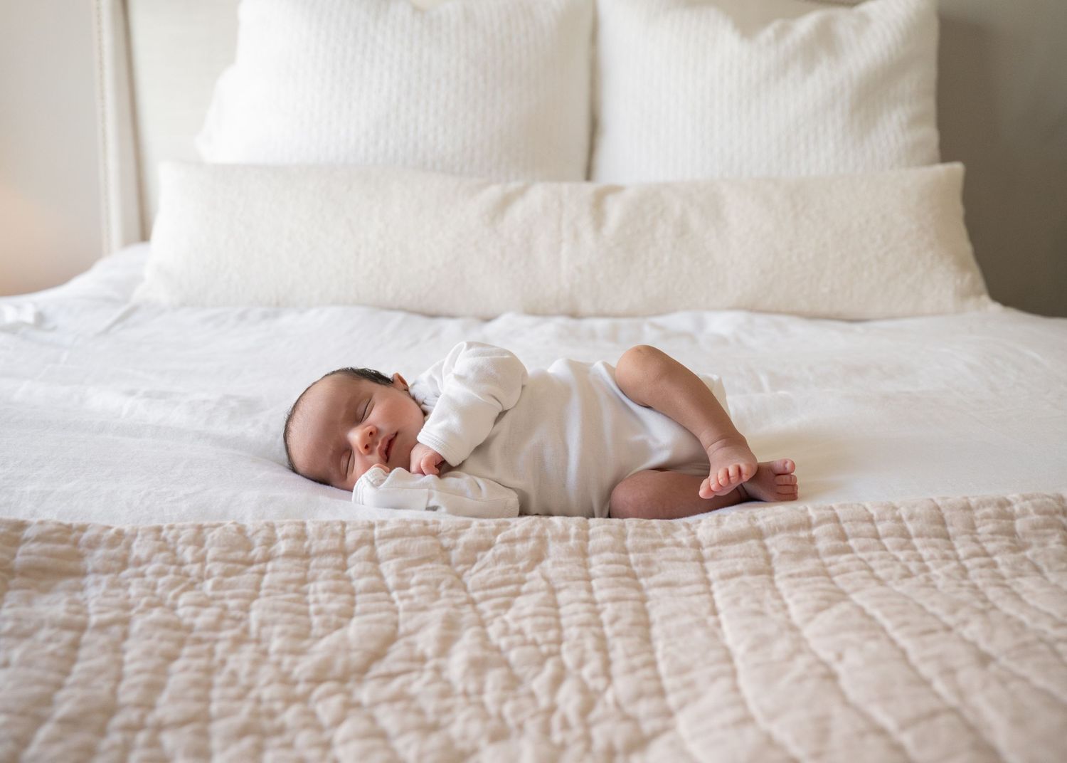 Artistic overhead view of sleeping newborn on white bed with pillows.