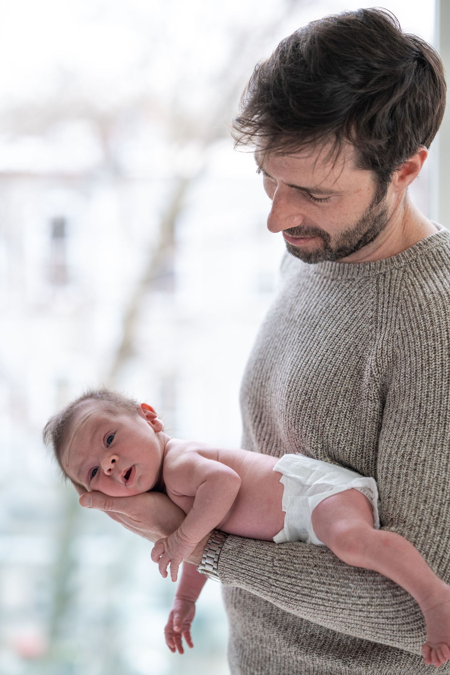Parent in gray sweater holding and cradling a newborn baby in white diaper.