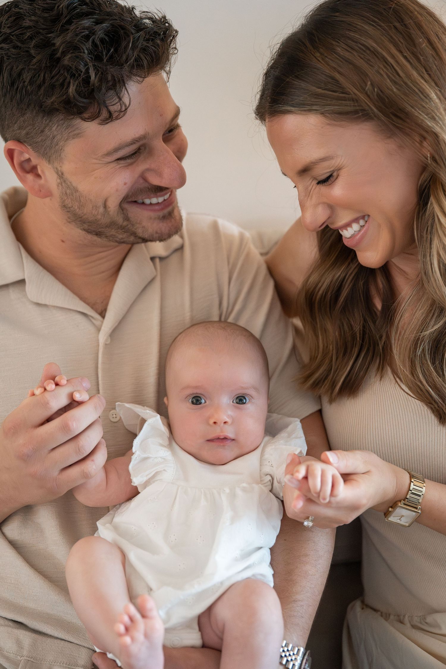 Warm family photoshoot showing parents cuddling with baby in neutral tones.