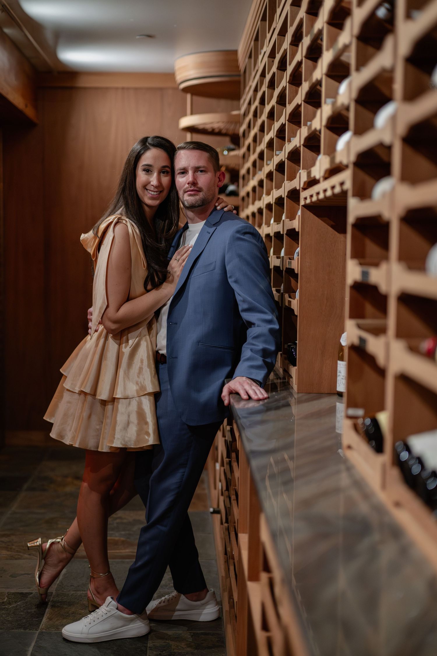 Couple poses intimately in a wine cellar with wooden wine racks creating a romantic ambiance.