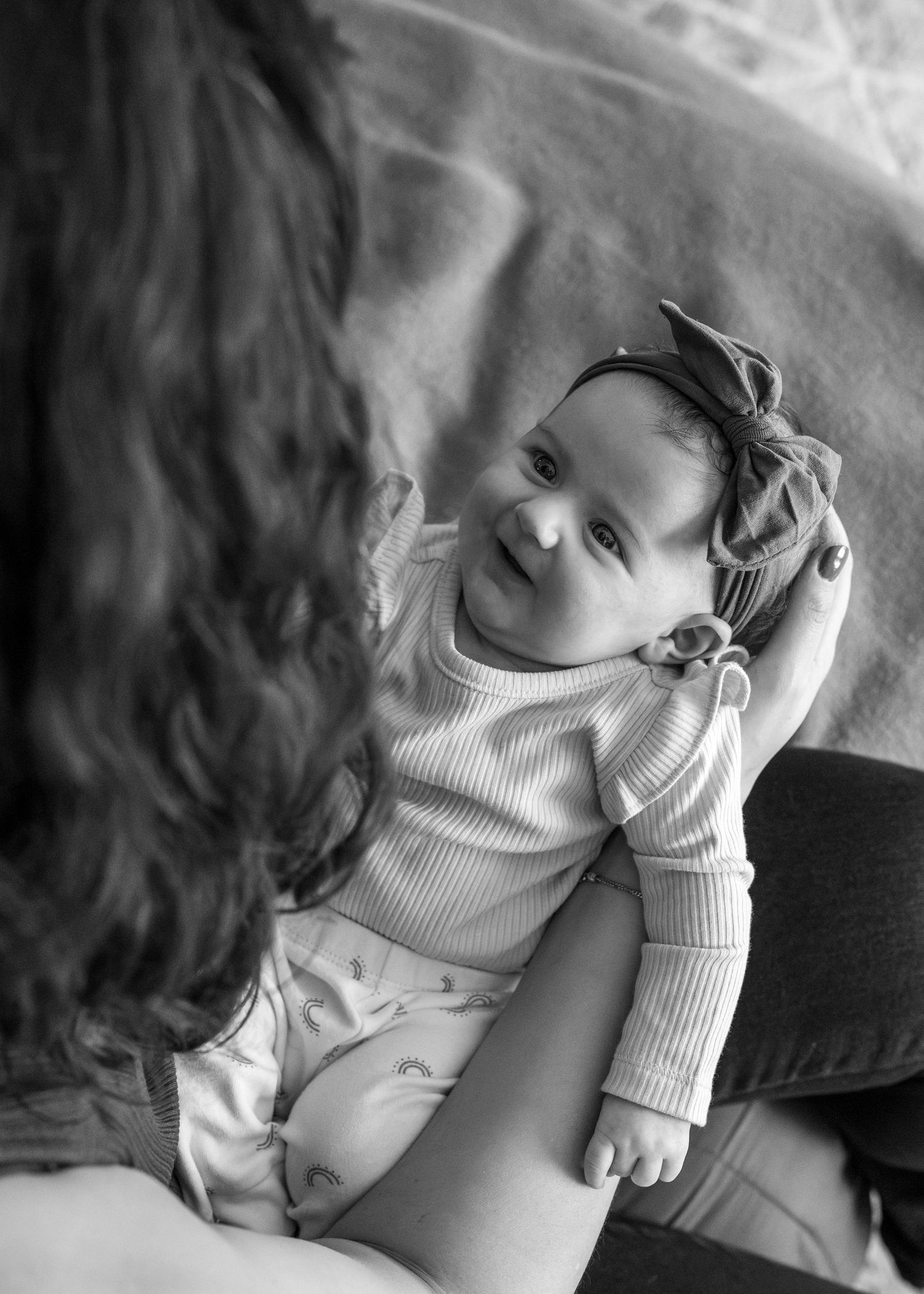 Black and white photo of a baby wearing a bow headband and ribbed sweater looking up at someone with a sweet expression.