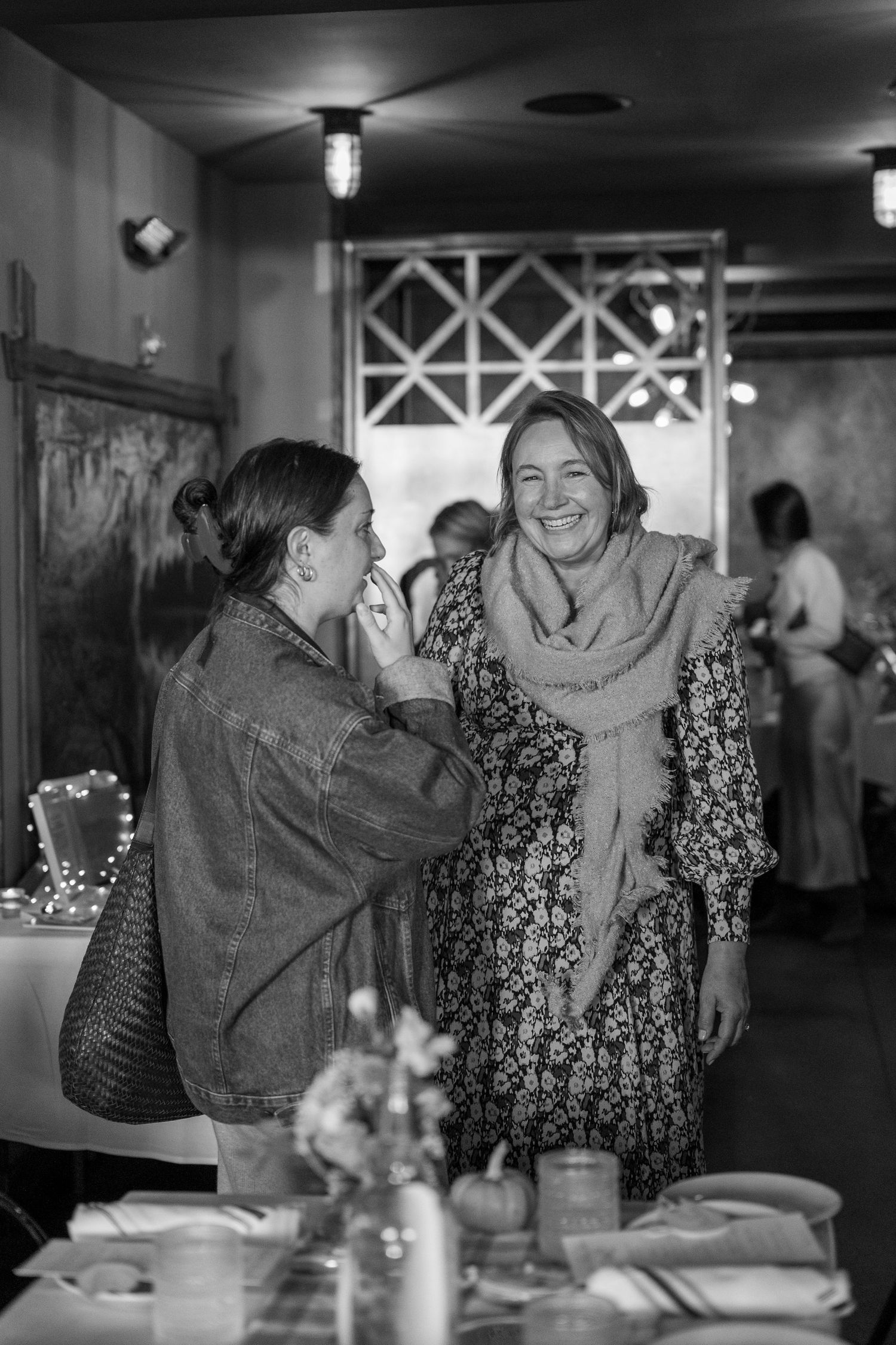 Friends sharing joyful moments and laughter at a restaurant table in black and white.