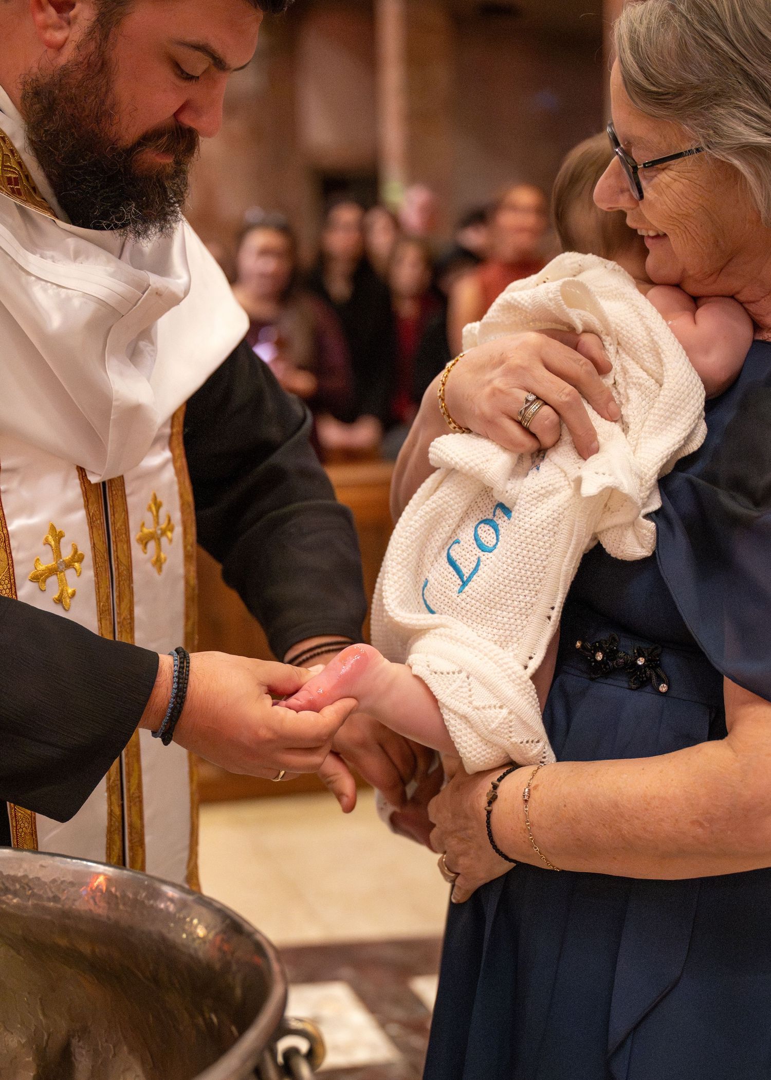 Baptism ceremony with priest and family gathered around baptismal font.