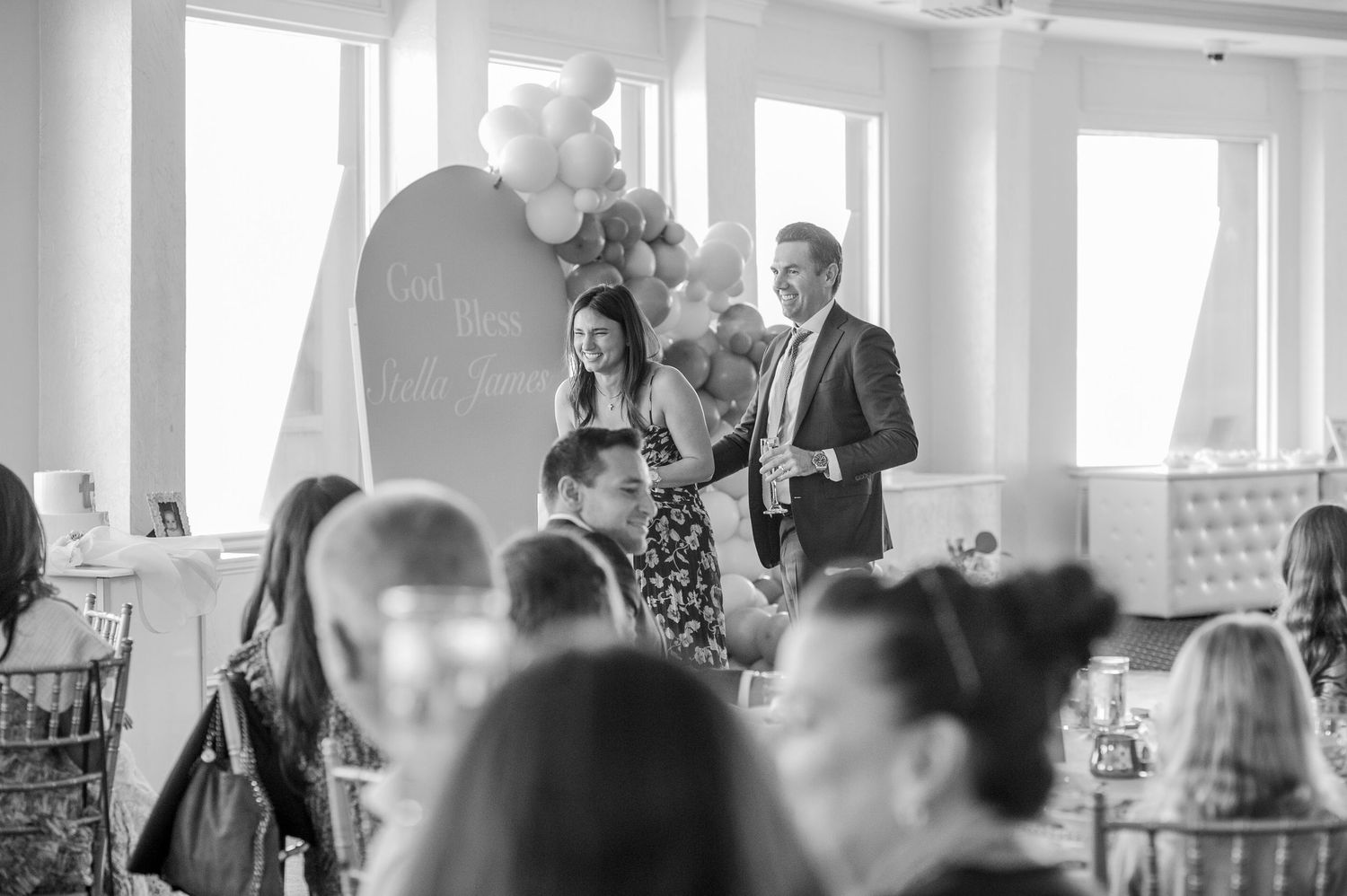 A black and white panoramic photo showing a group of people gathered in a bright interior space for a social event.