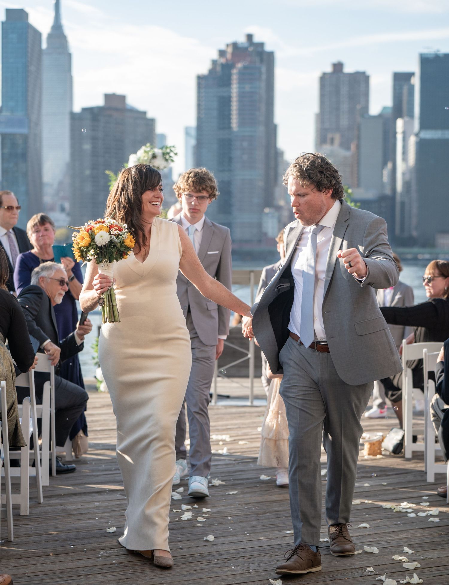 Wedding guests form a receiving line on a pier with the New York City skyline in the background.
