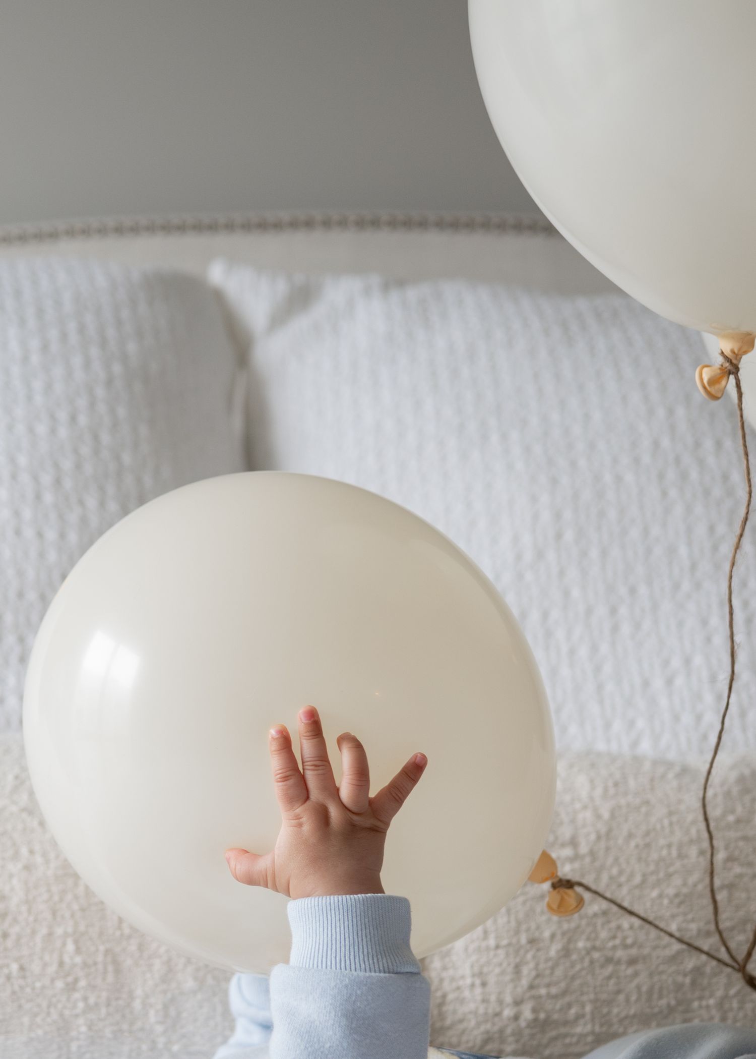 Baby hand reaching out to touch a large cream white balloon with another balloon in the background.